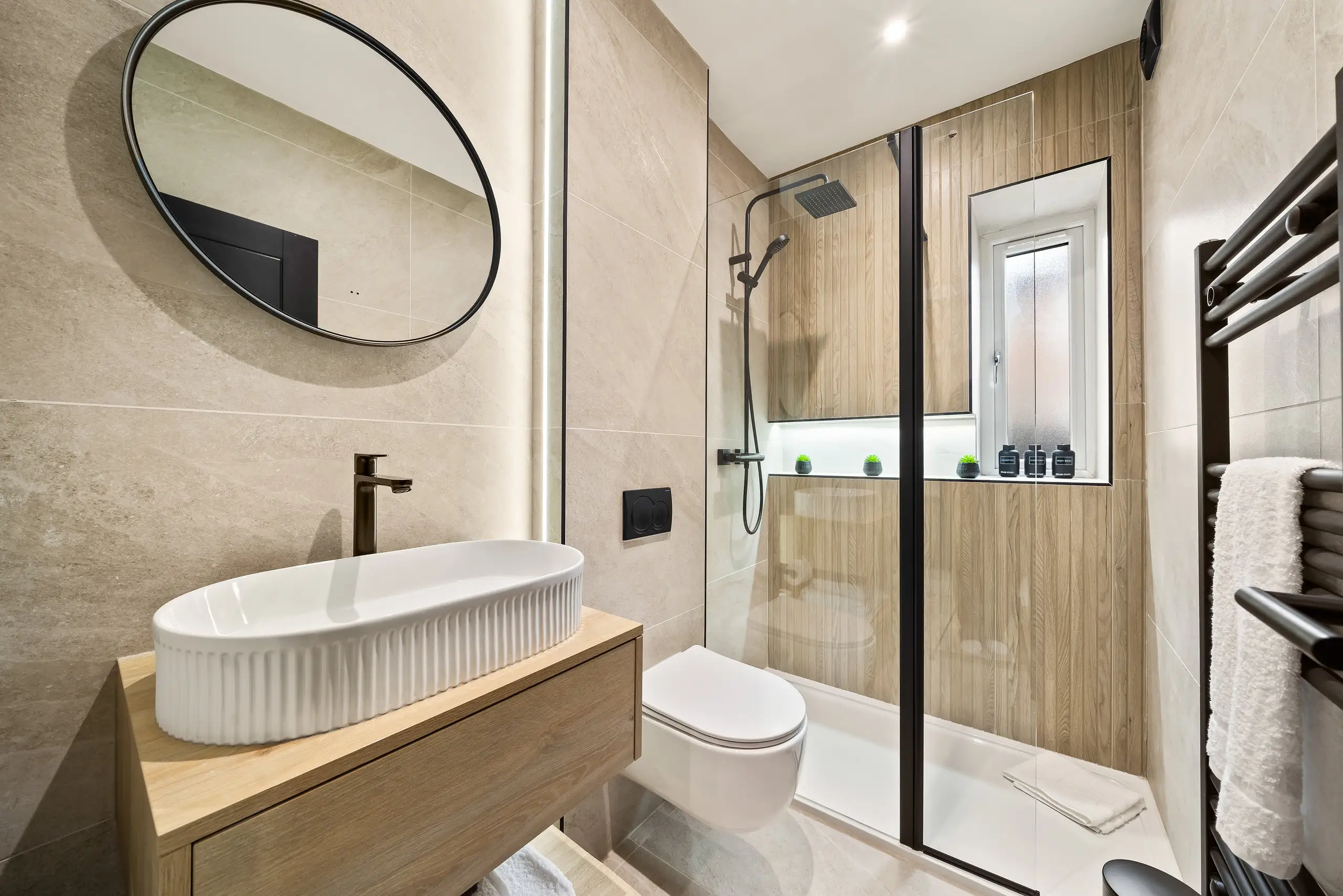 Shower room with a fluted basin on a wooden vanity, round mirror, walk-in shower and heated towel rail