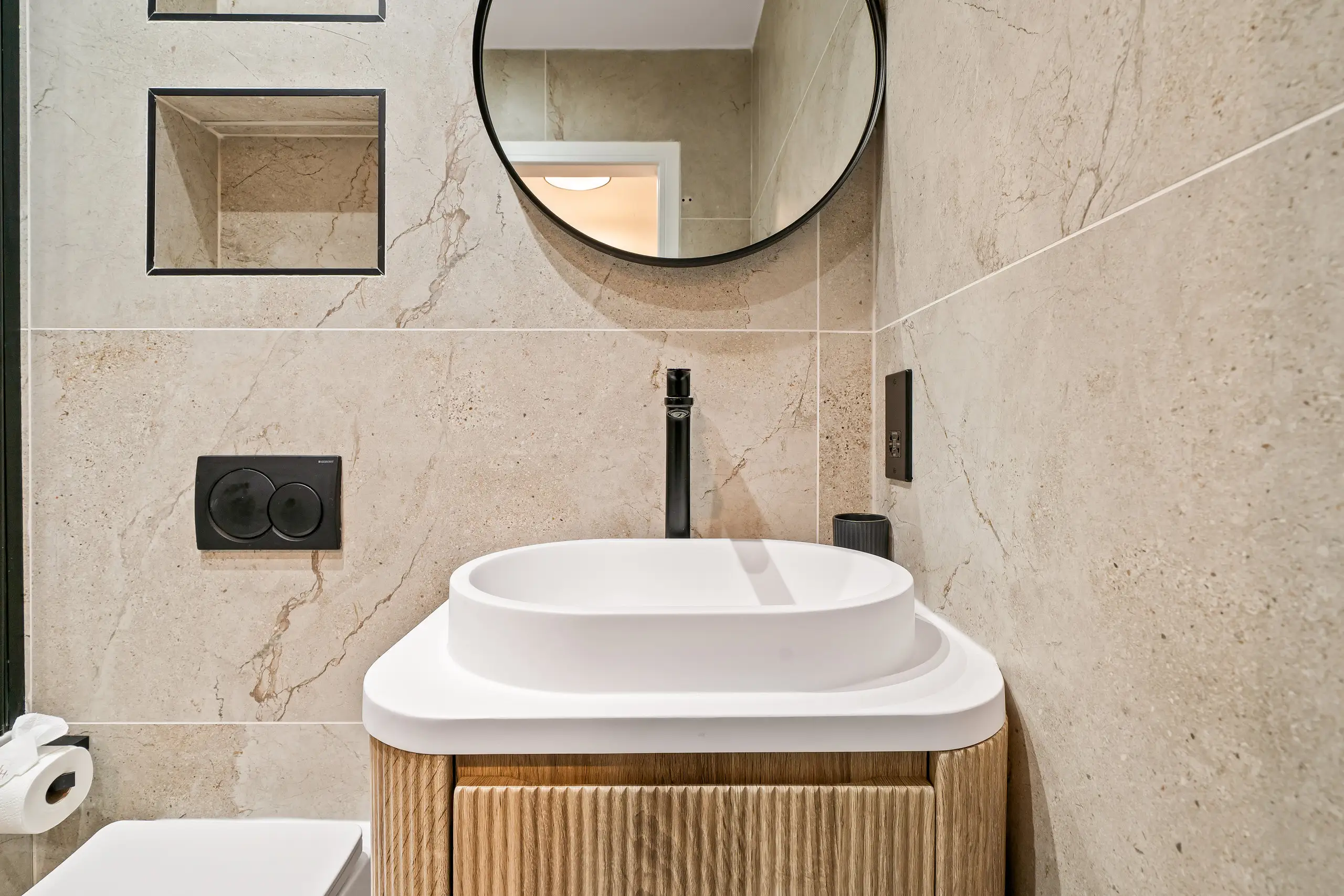 Close view of a fluted wooden vanity with a white basin, black tap and stone-effect tiles