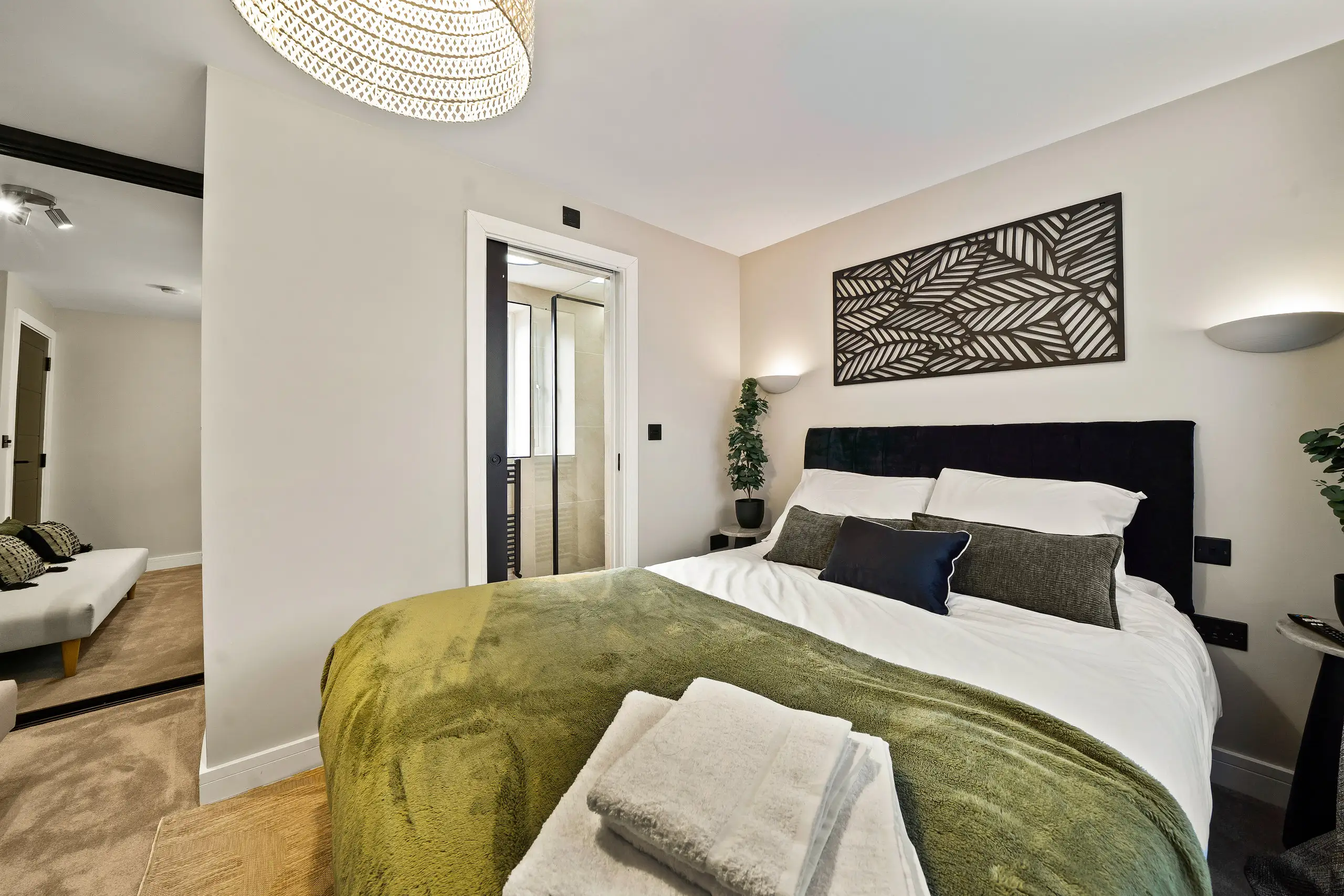 Double bedroom with an olive throw, black headboard and decorative wall panel, with an open door to a shower room