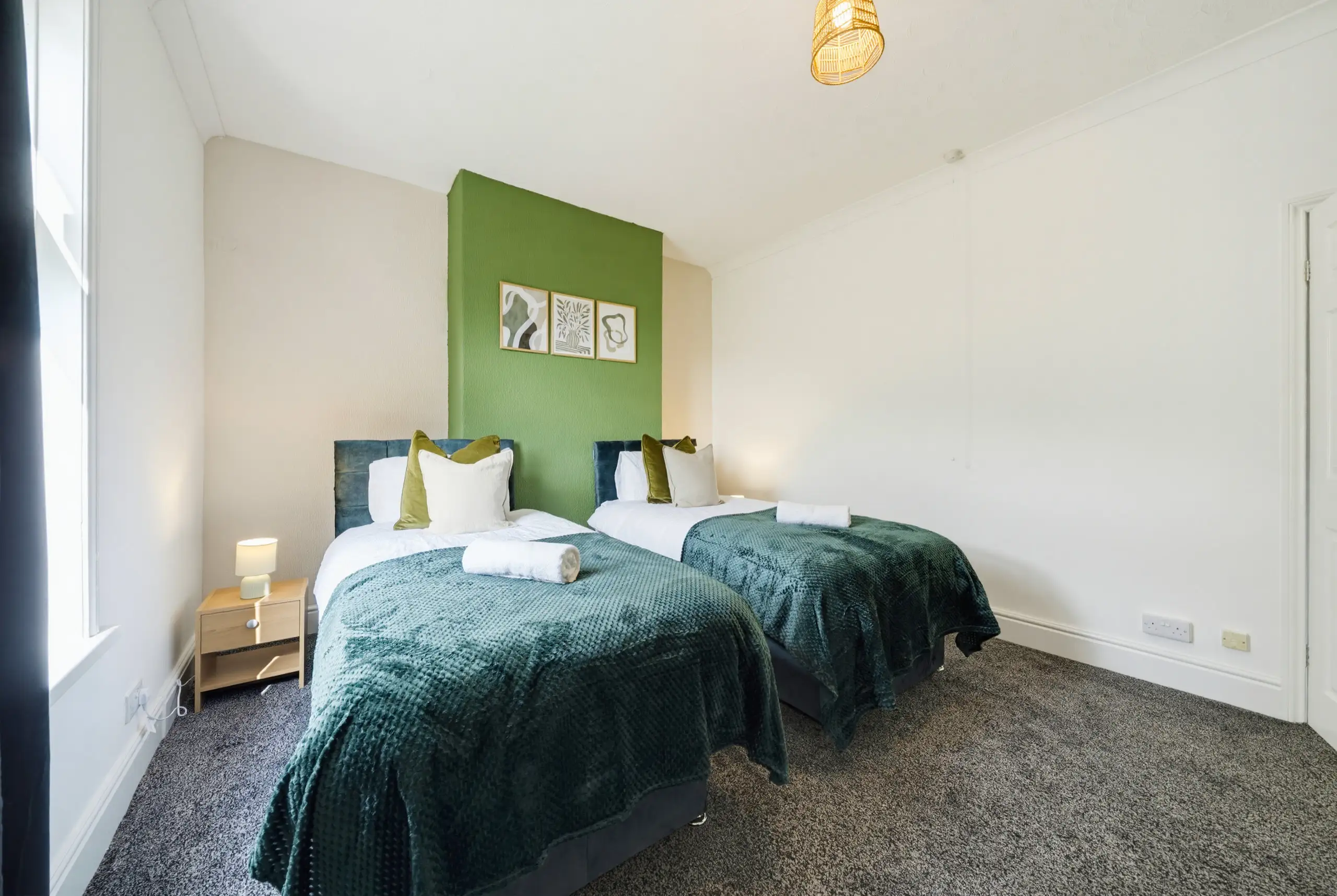 Twin bedroom with teal throws, a green feature wall and three framed prints
