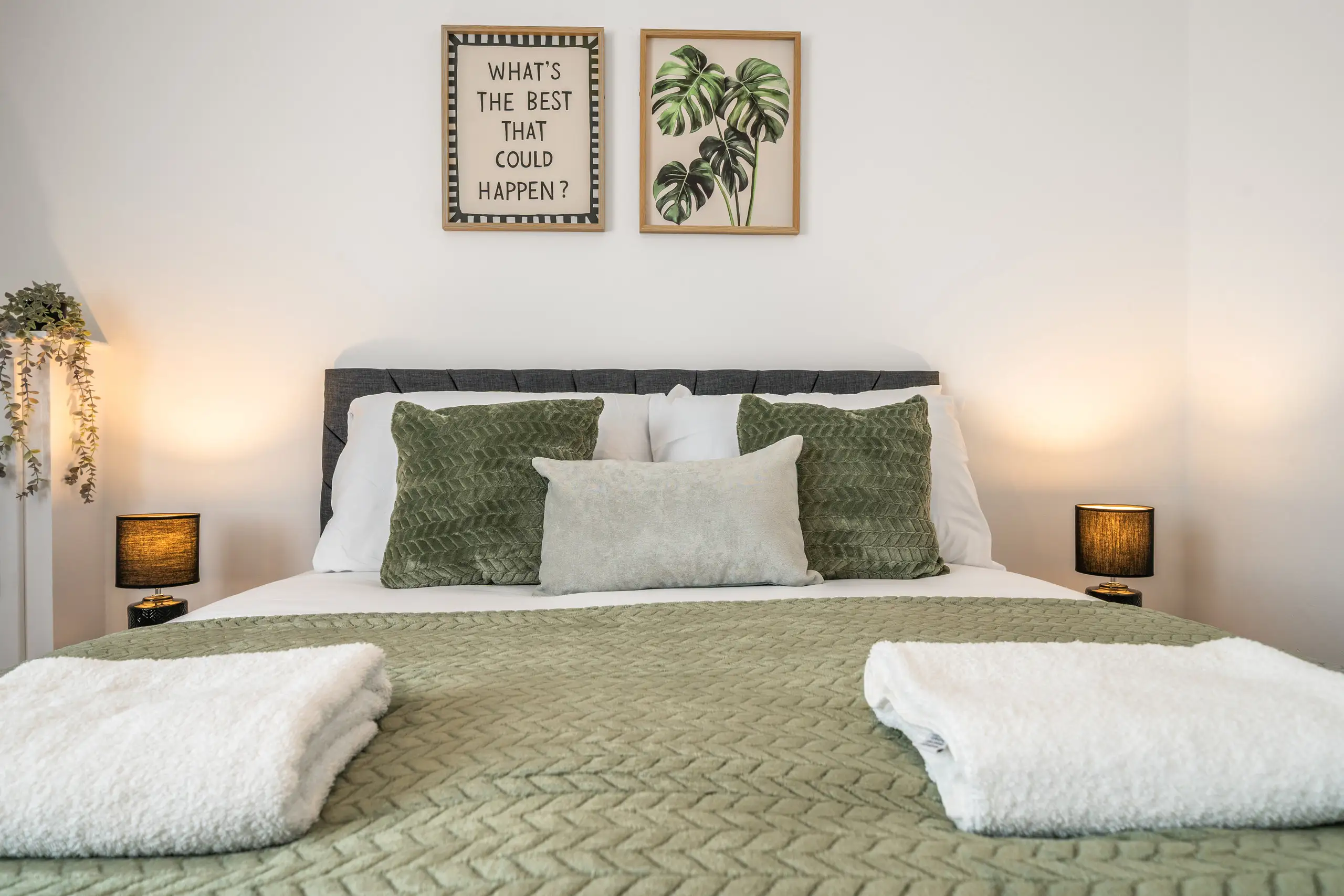 Double bedroom with a green throw, folded white towels and lit bedside lamps