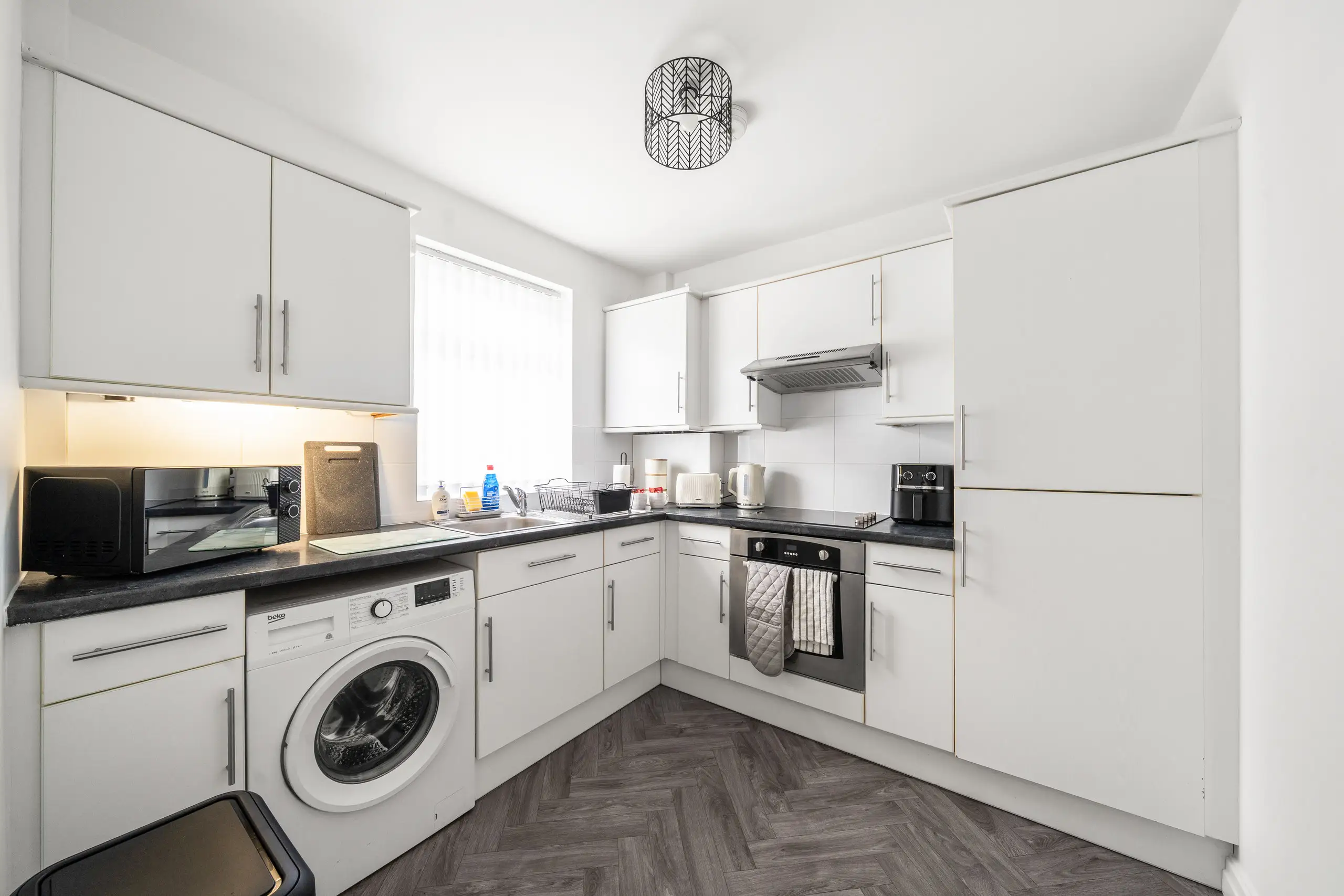 White kitchen with a herringbone floor, washing machine and built-in oven