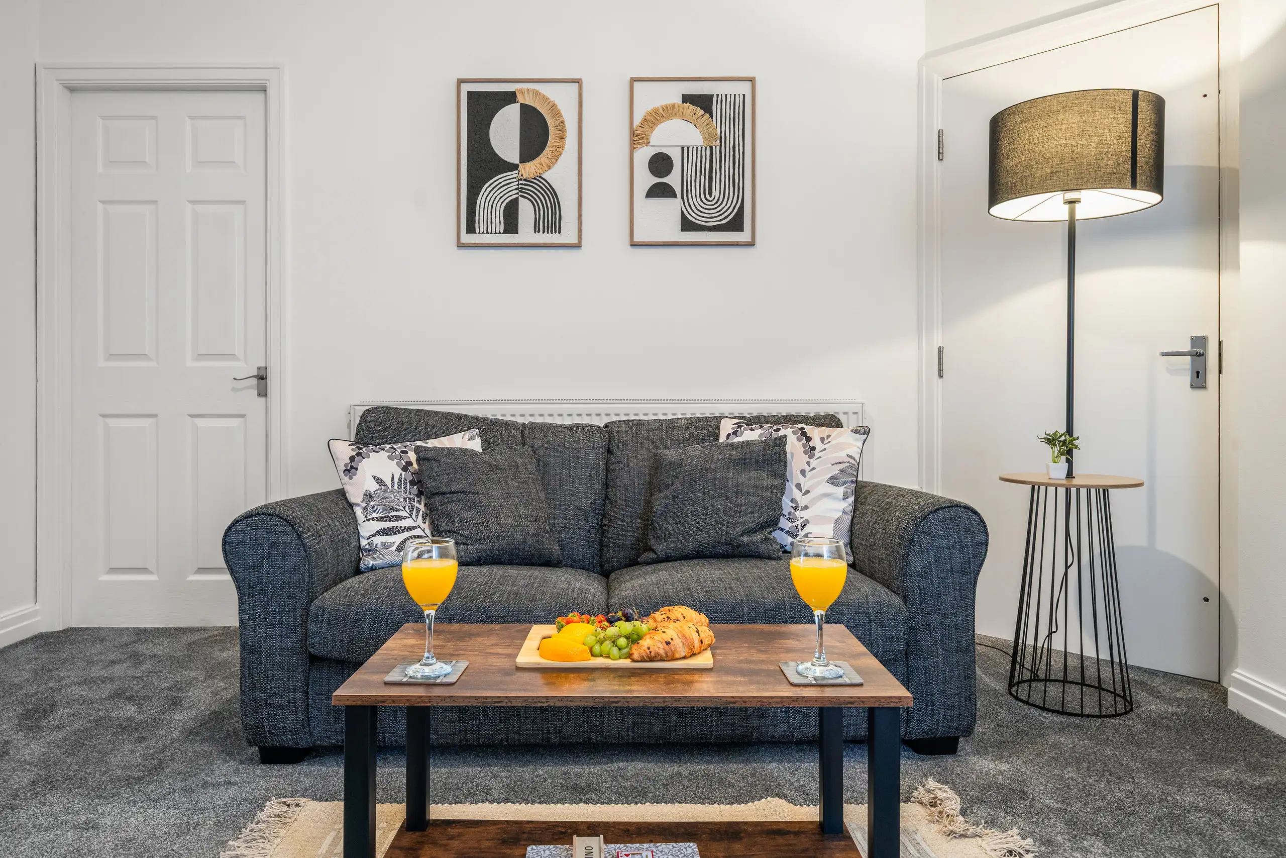 Living room with a grey sofa, two framed prints and a coffee table set with orange juice and fruit