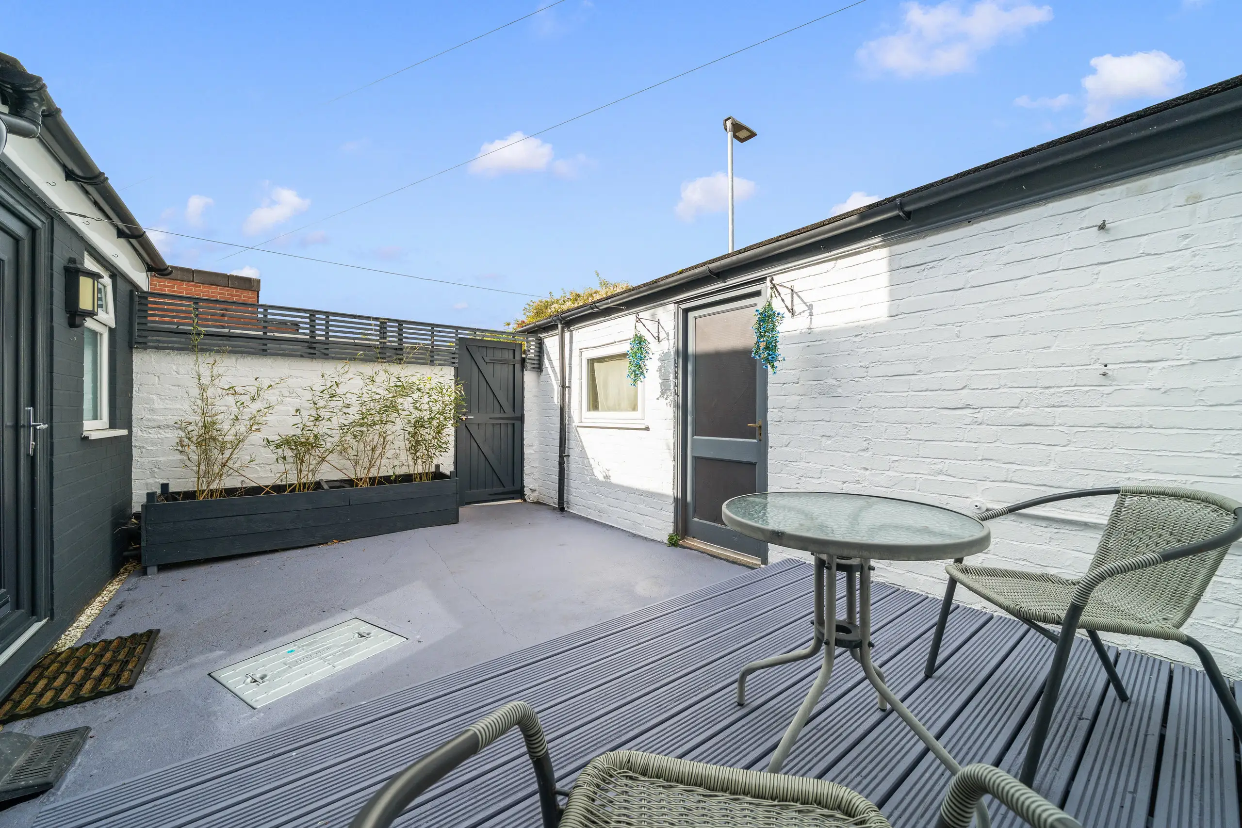 Courtyard with decking, a glass table and two chairs between white-painted brick walls