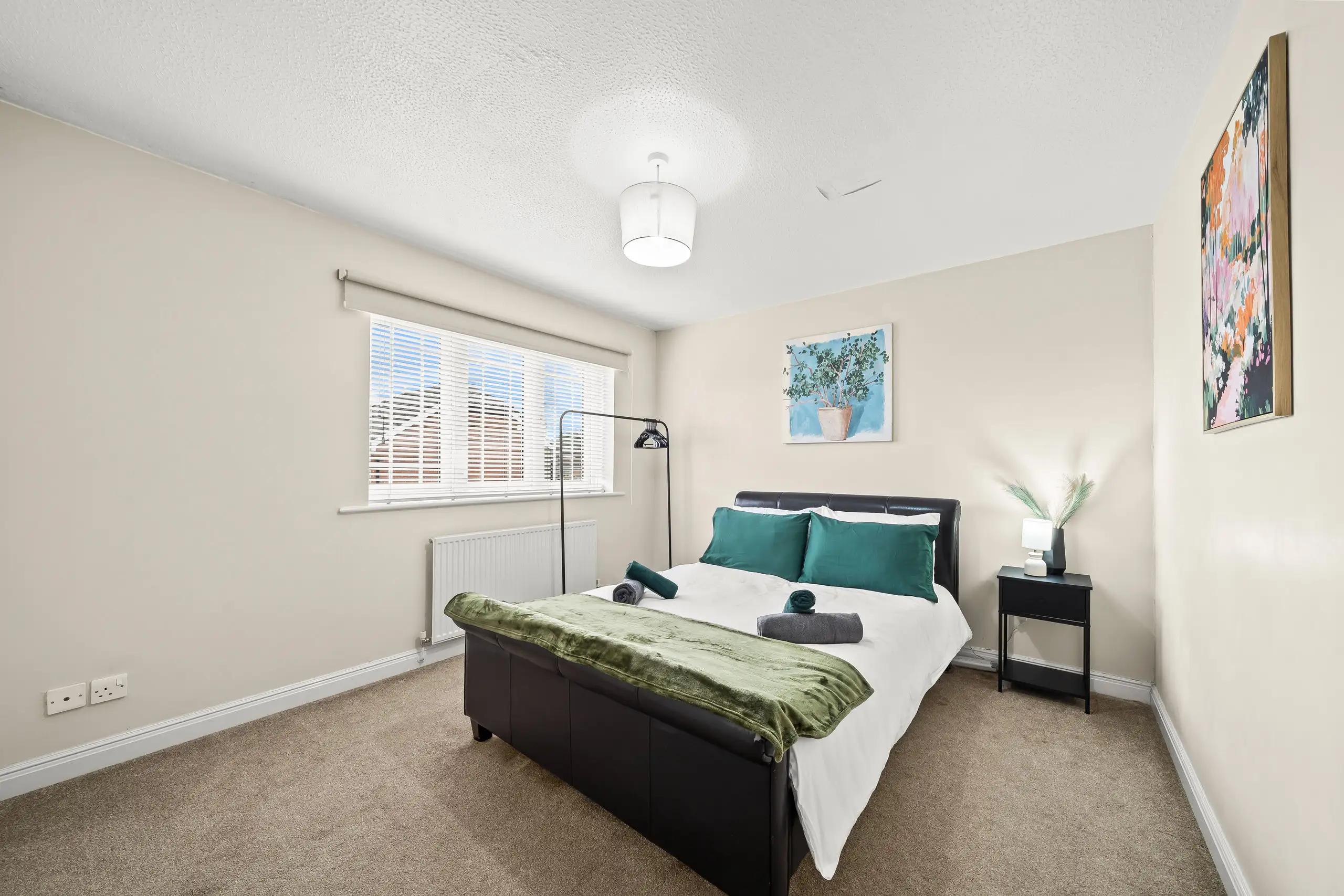 Double bedroom with teal pillows, a green throw and a black leather bed frame