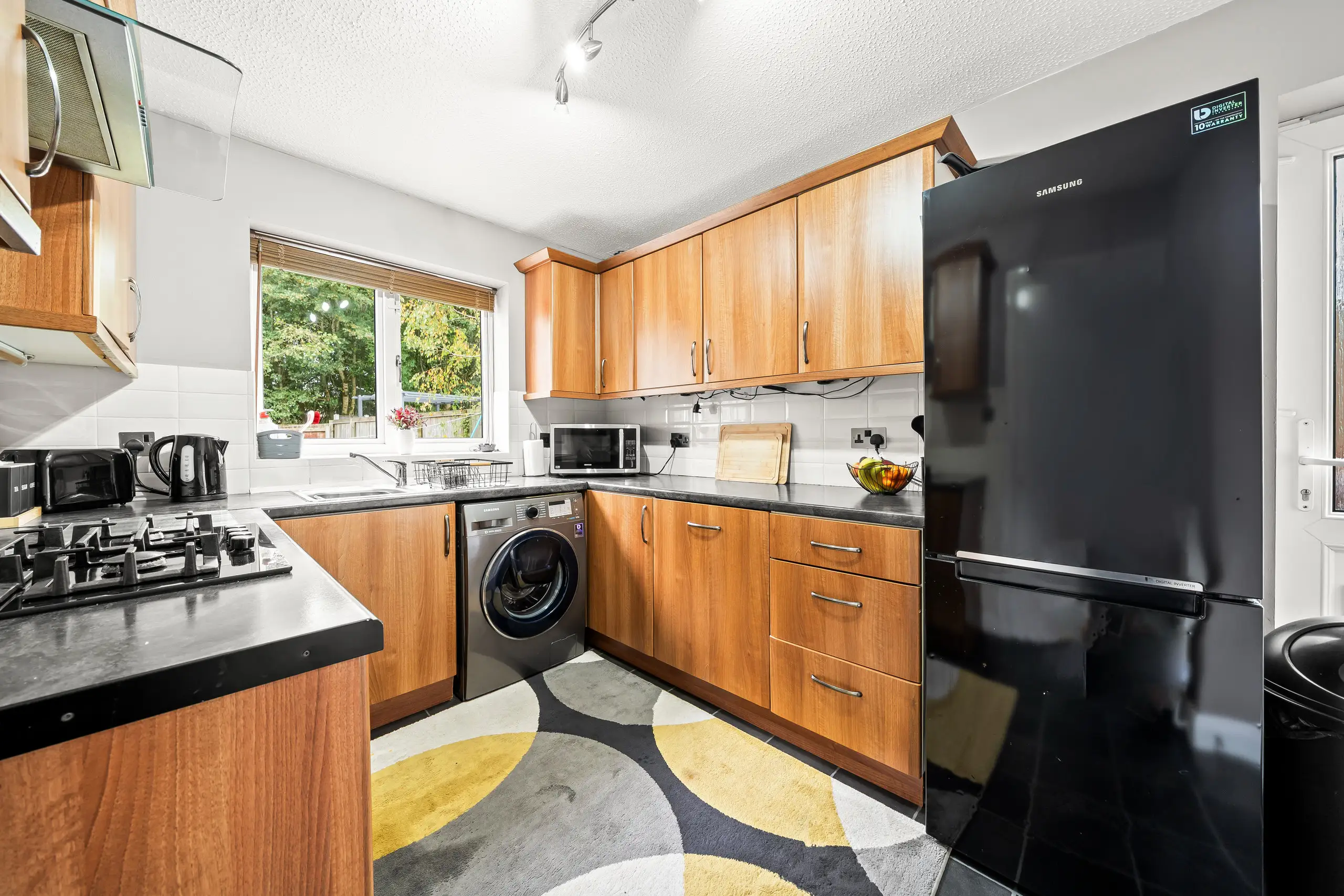 Kitchen with wood-effect units, black worktops, a black fridge freezer and a patterned floor