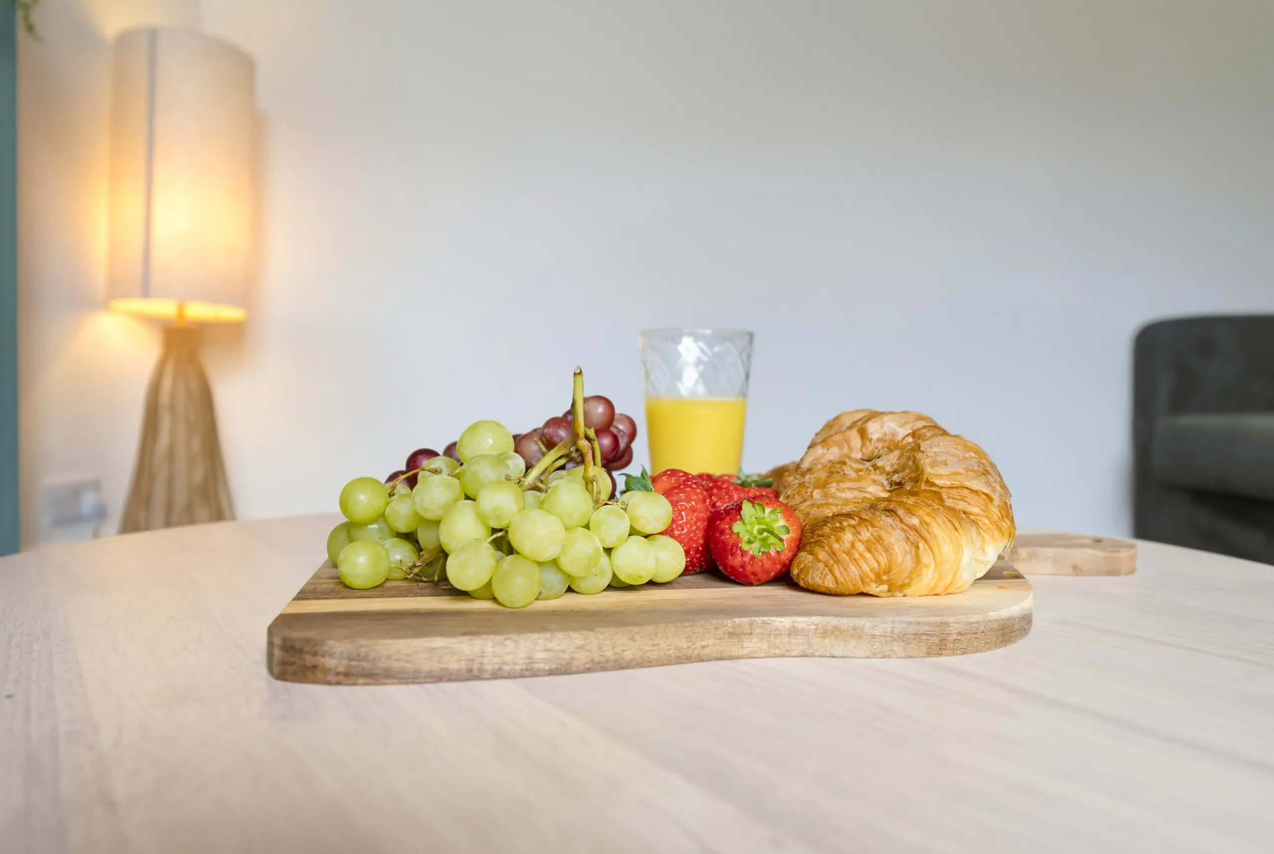 Grapes, strawberries, croissants and orange juice on a wooden board