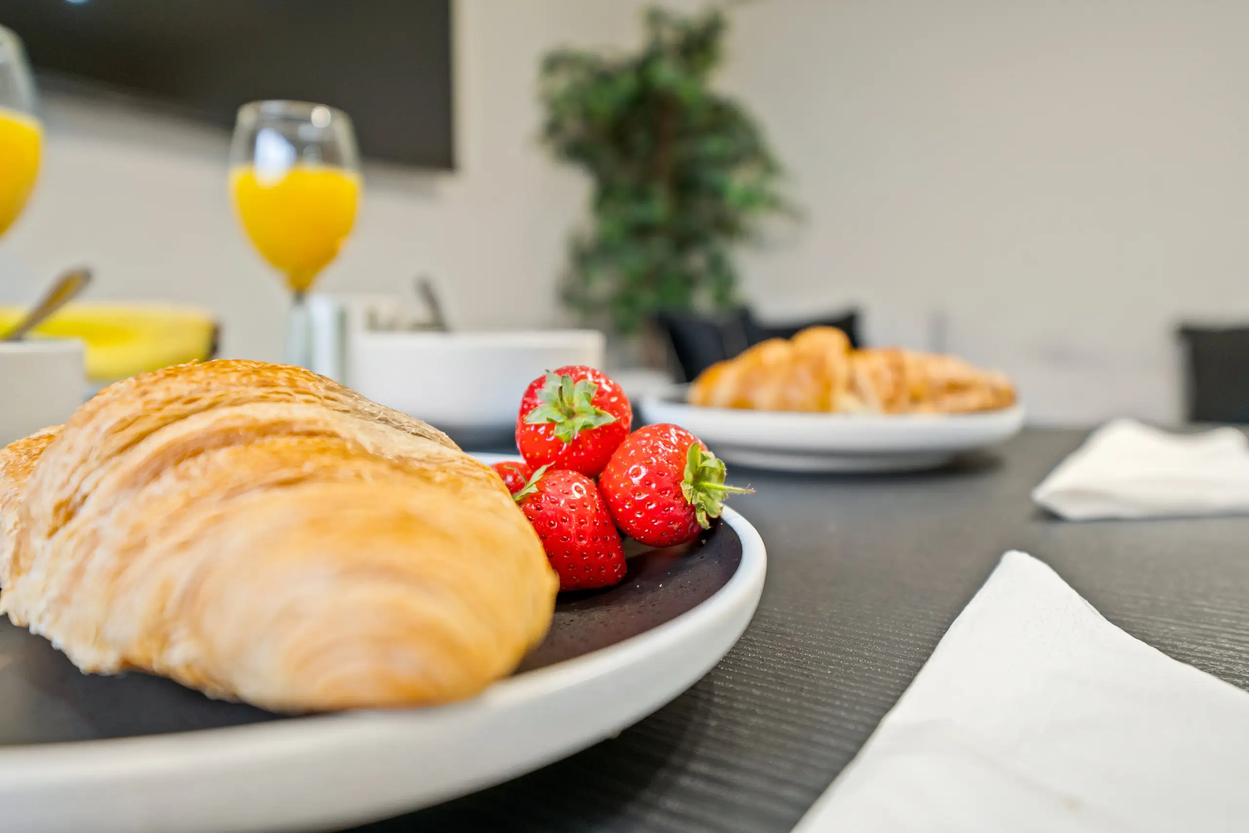 Close-up of a croissant and strawberries on a plate, with orange juice behind
