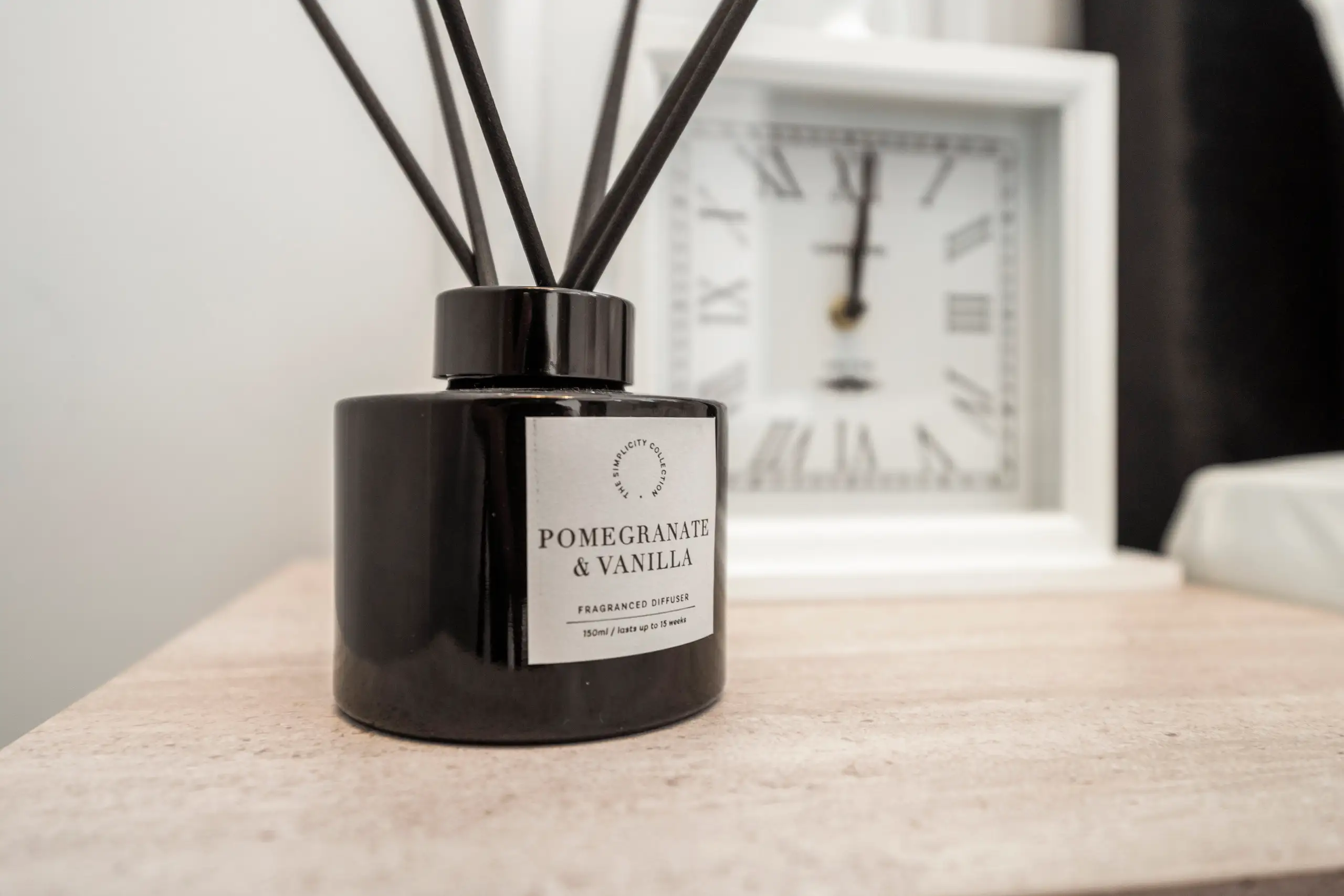 Reed diffuser and a white clock on a bedside table