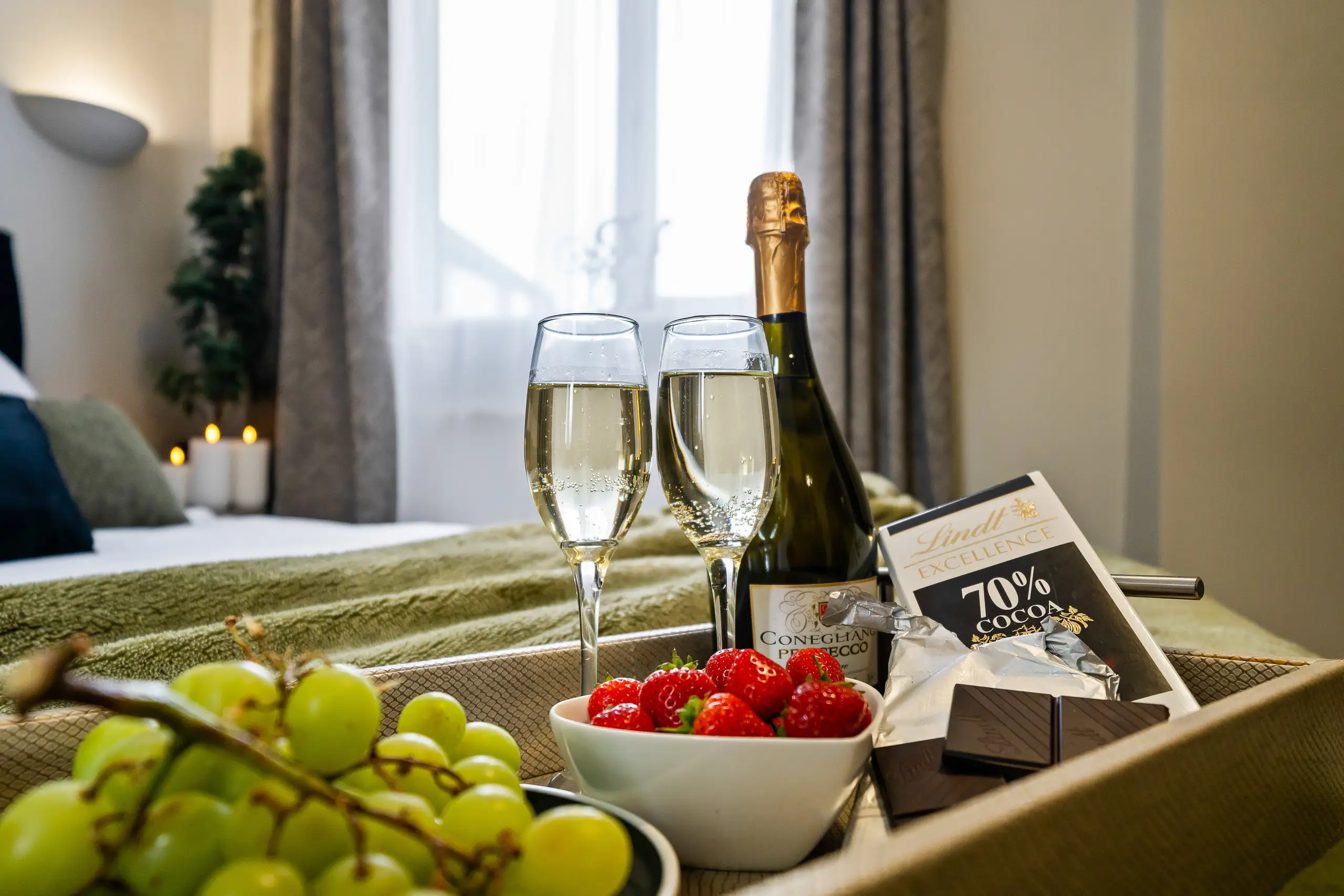 Welcome tray on a bed with prosecco, two glasses, grapes, strawberries and chocolate