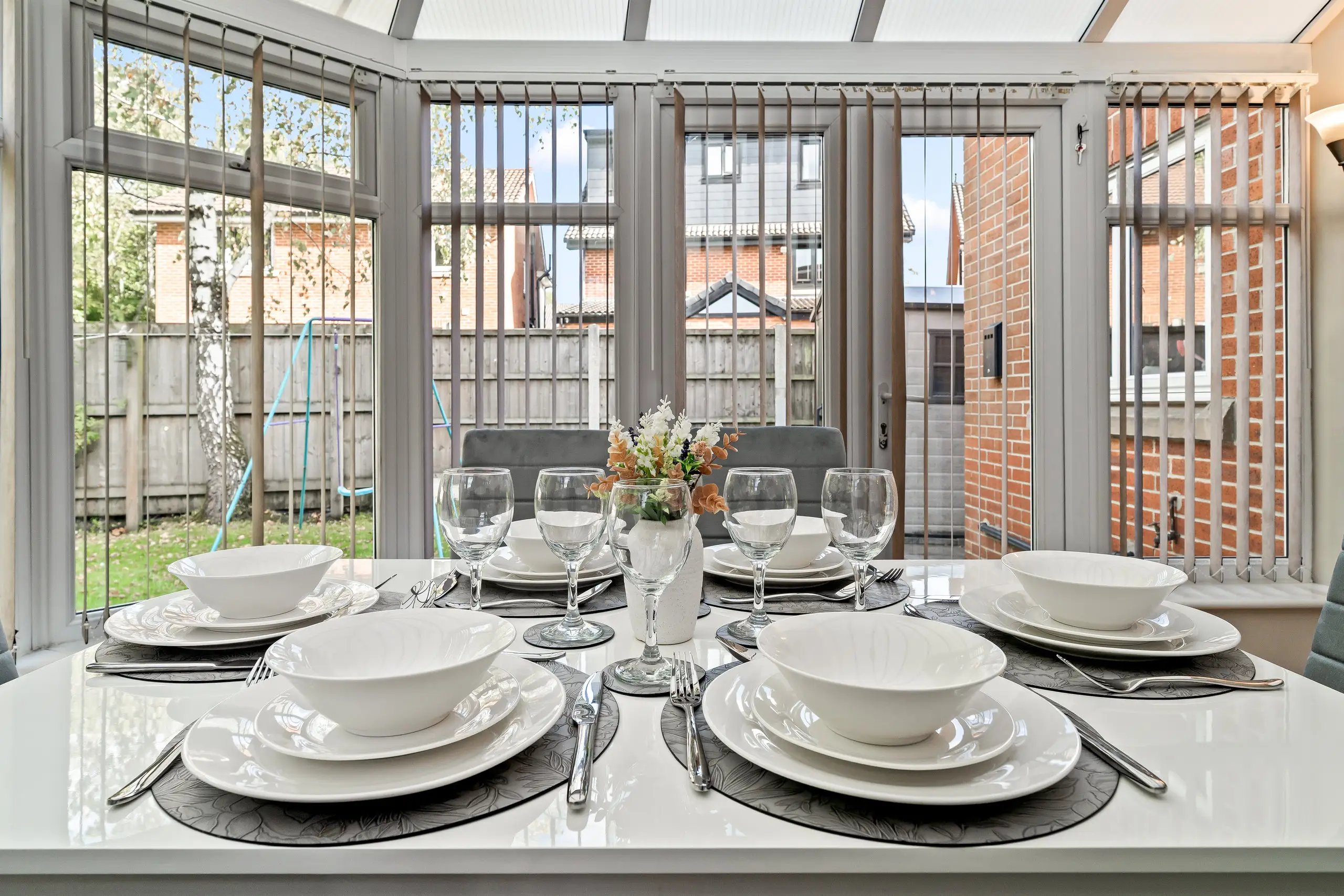 Table laid for six in a conservatory, with the garden visible through the windows
