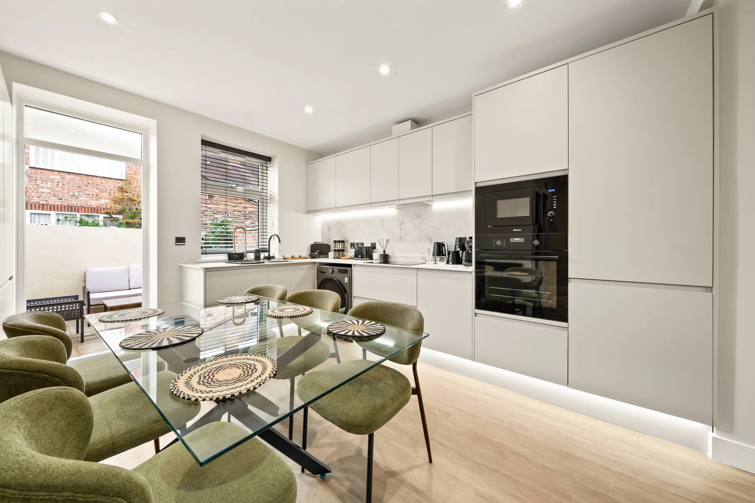 Kitchen and dining area with a glass table, green chairs, handleless units and a door out to a patio