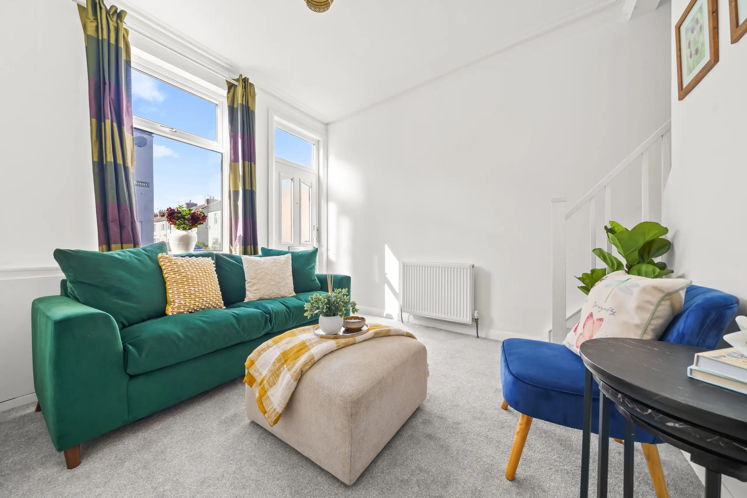 Living room with a green velvet sofa, upholstered footstool, blue armchair and tall windows