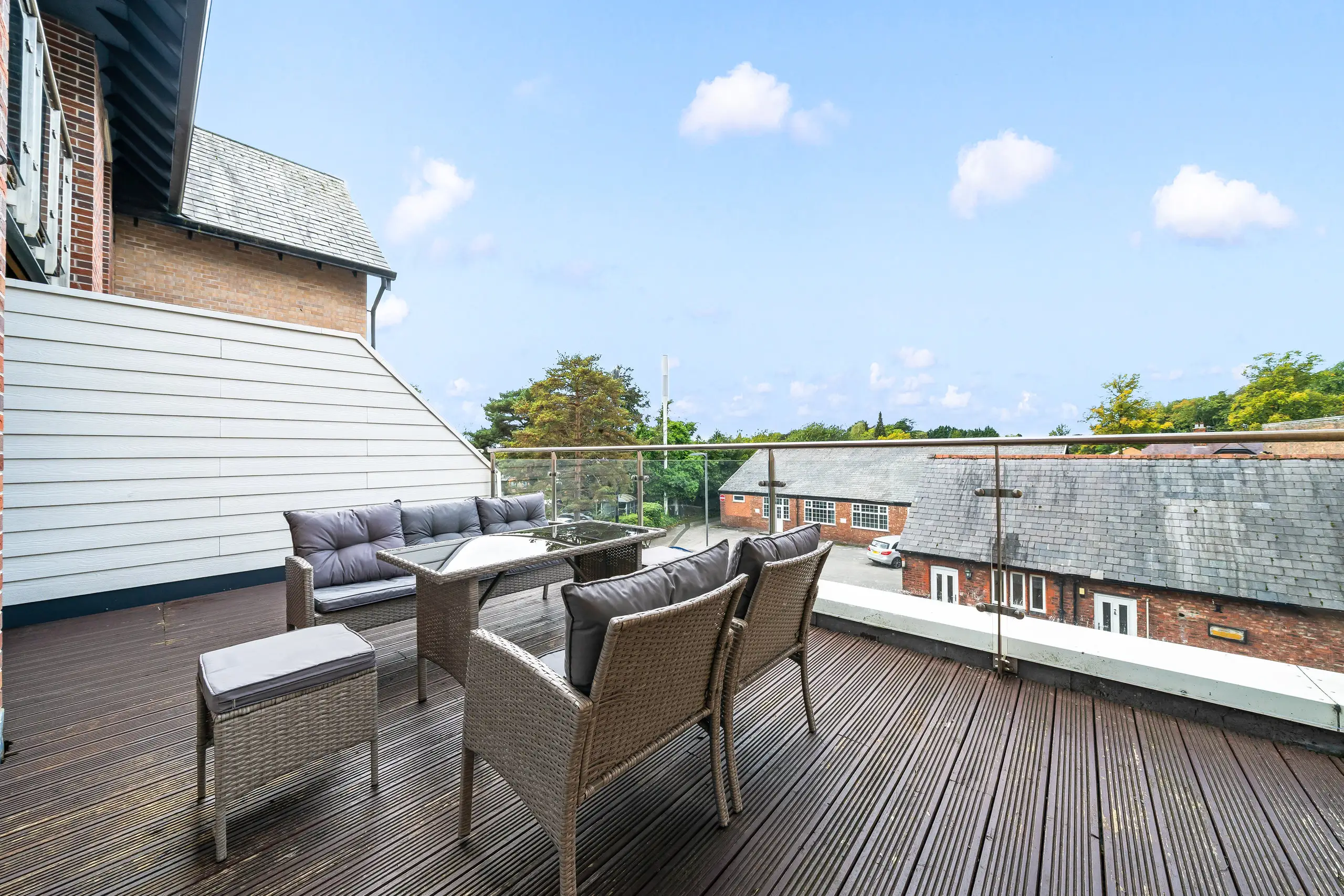 Roof terrace with rattan seating, decking and a glass balustrade under a blue sky