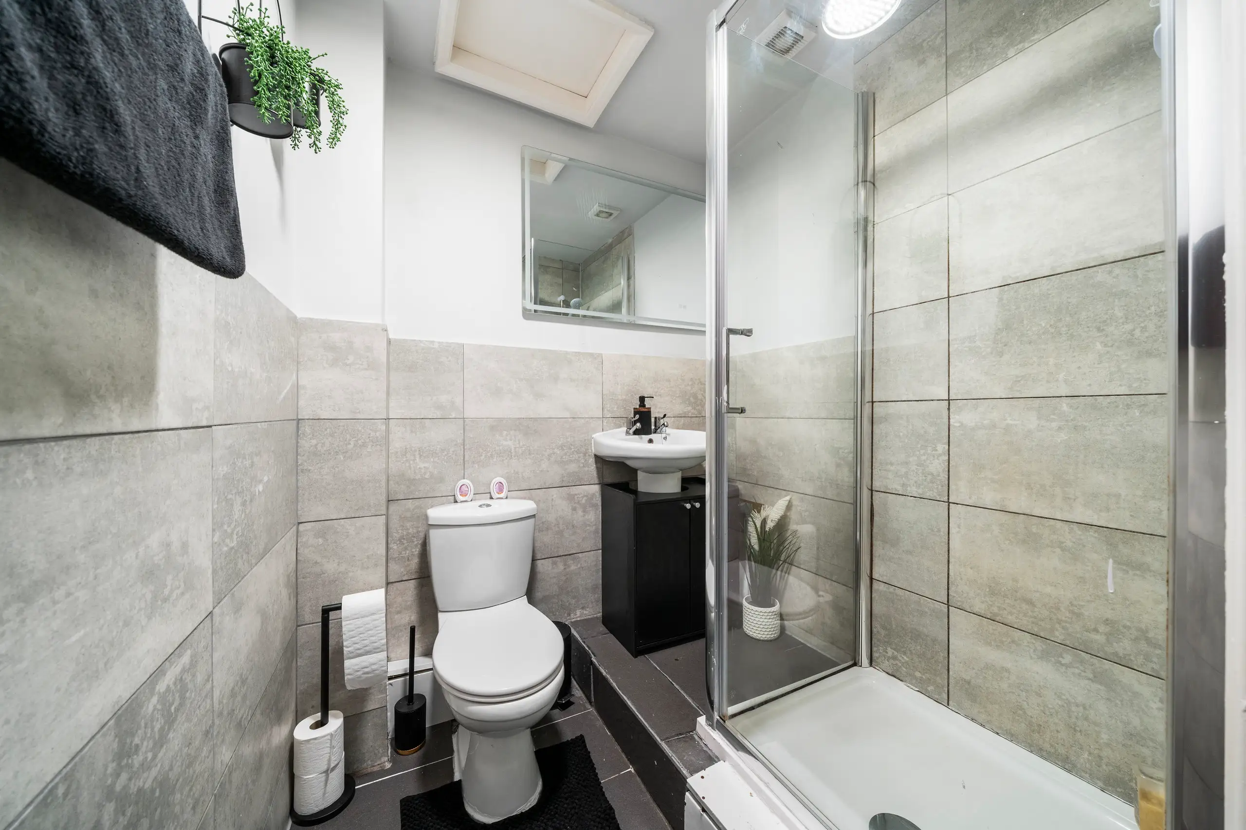 Shower room with large grey tiles, a corner shower and a small basin