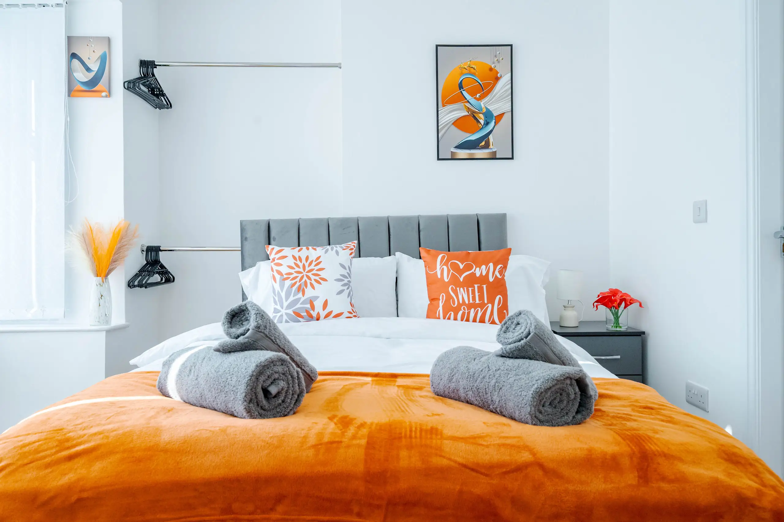 Double bedroom with a burnt orange throw, rolled grey towels and orange cushions