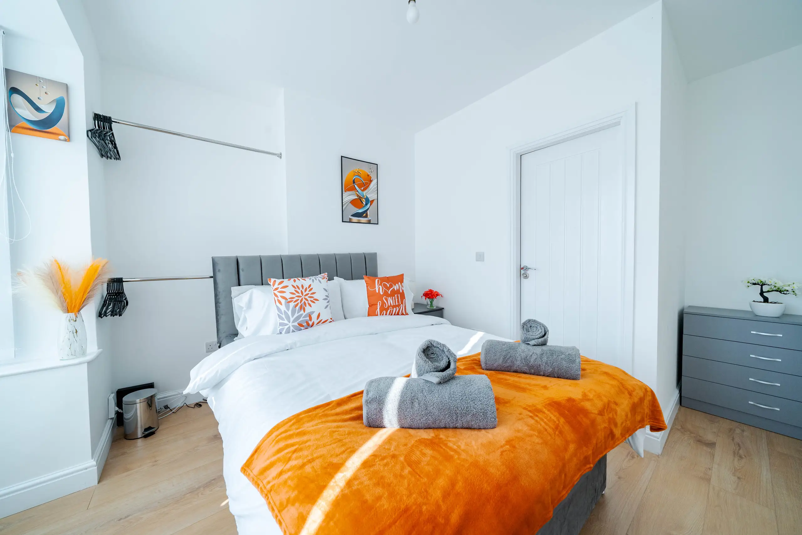 Wider view of the double bedroom with grey drawers, hanging rails and a white door