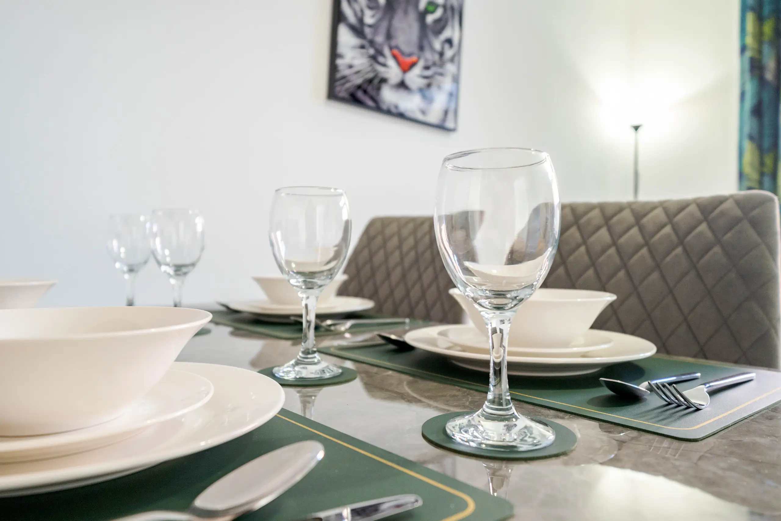Close view of a dining table set with bowls and wine glasses, a tiger print on the wall behind