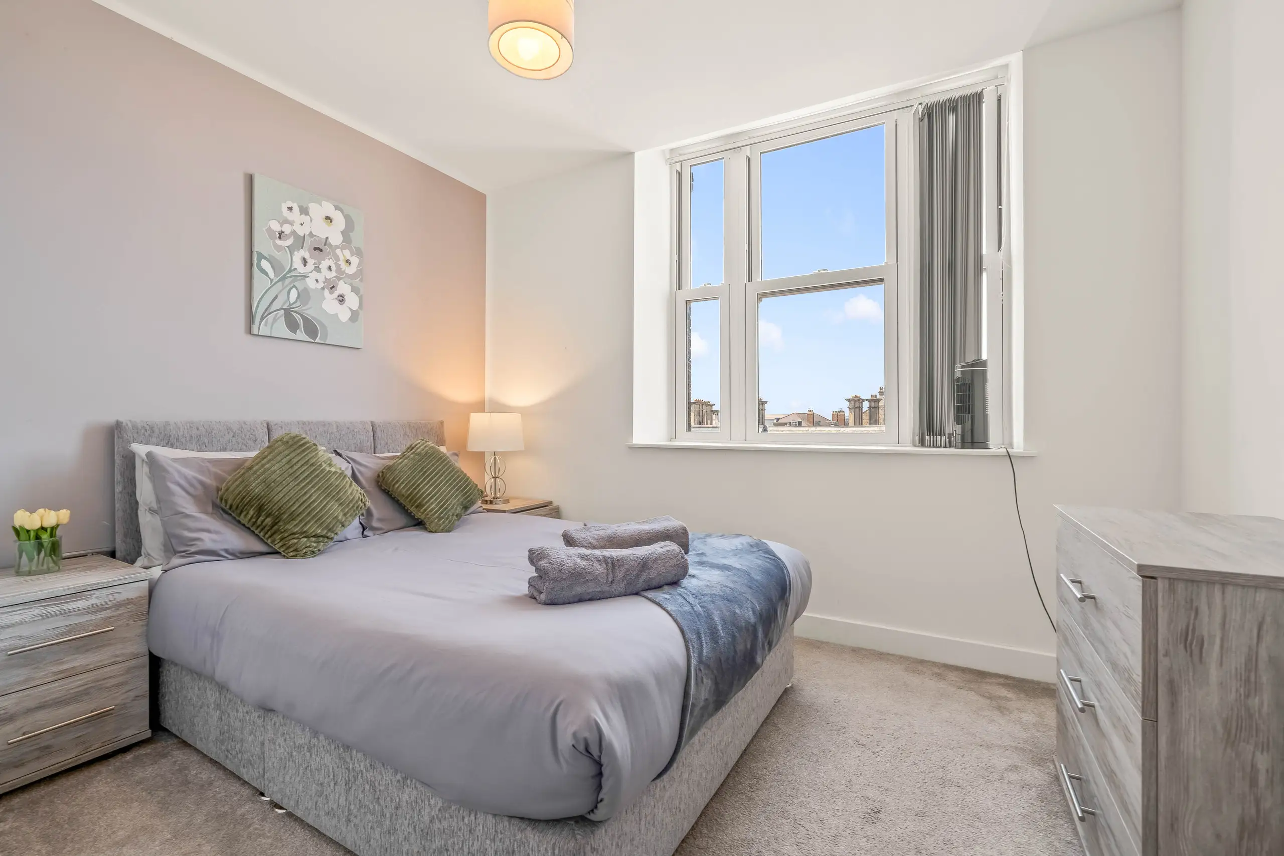 Double bedroom with a grey upholstered bed, green cushions and tall sash windows