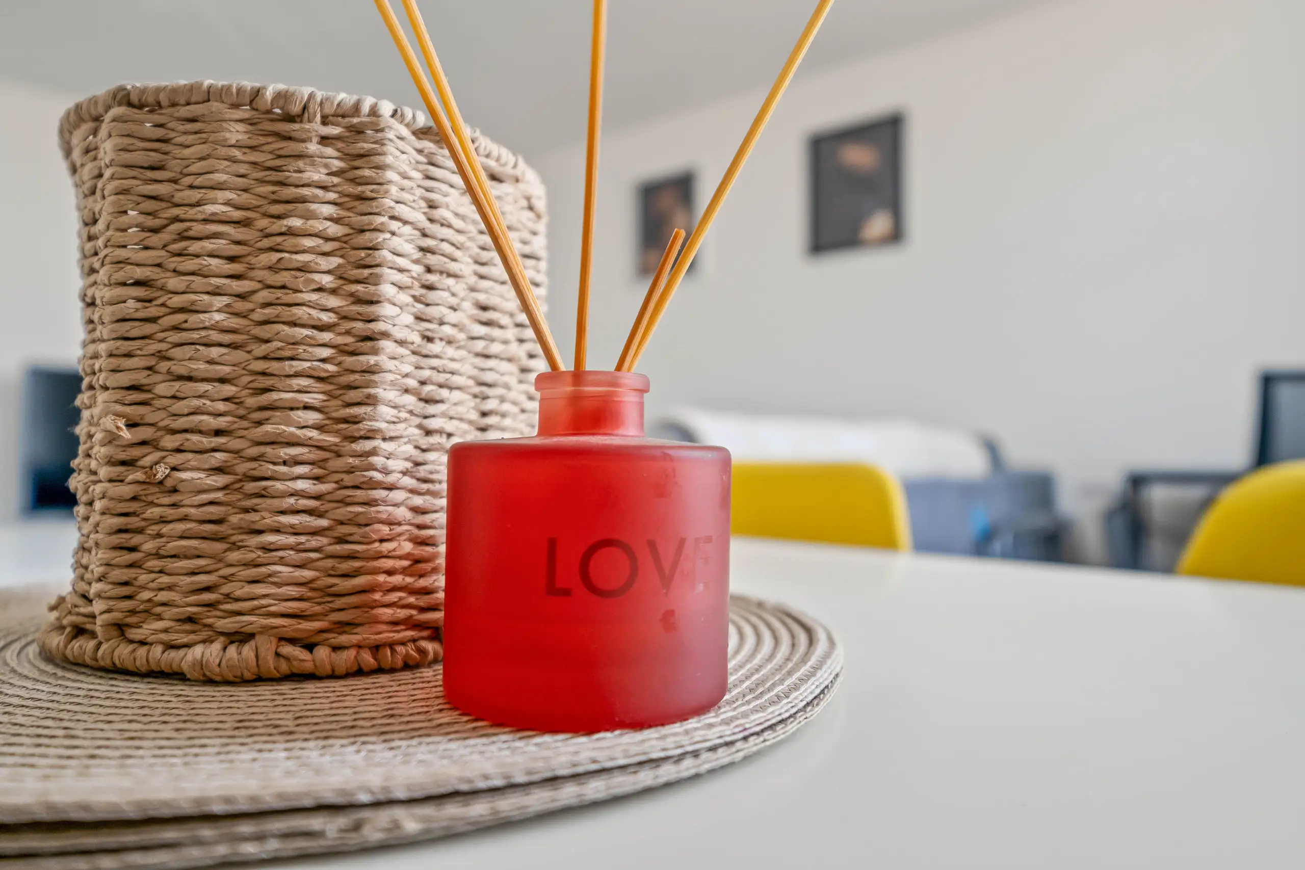 Red reed diffuser and woven basket on a white dining table