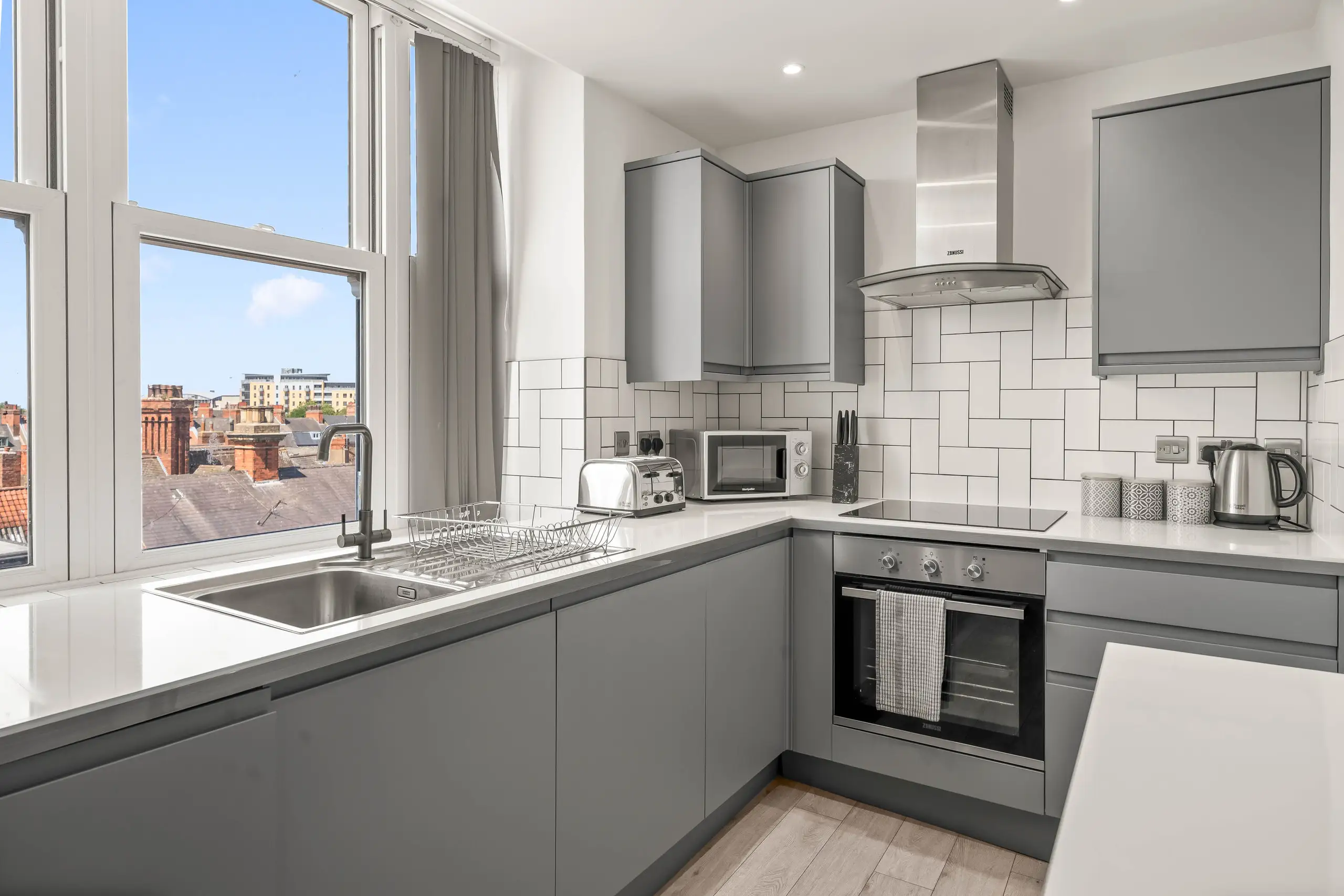Grey kitchen with white metro tiles and tall windows looking over rooftops