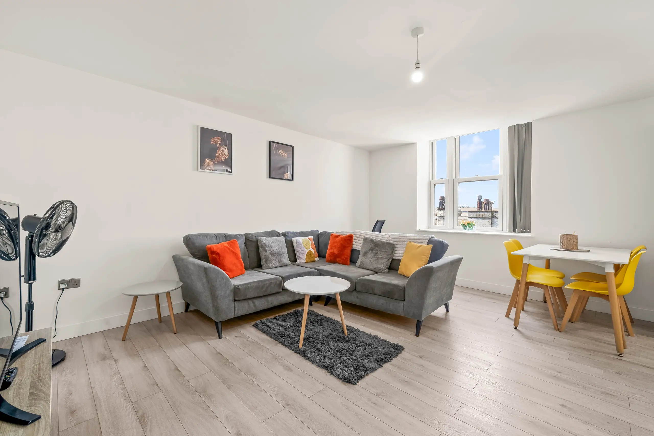 Open-plan living area with a grey corner sofa, orange cushions and a dining table with yellow chairs