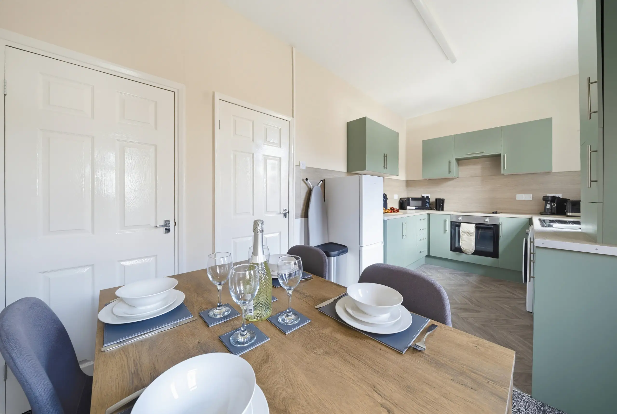 Dining table laid for four beside a sage green kitchen