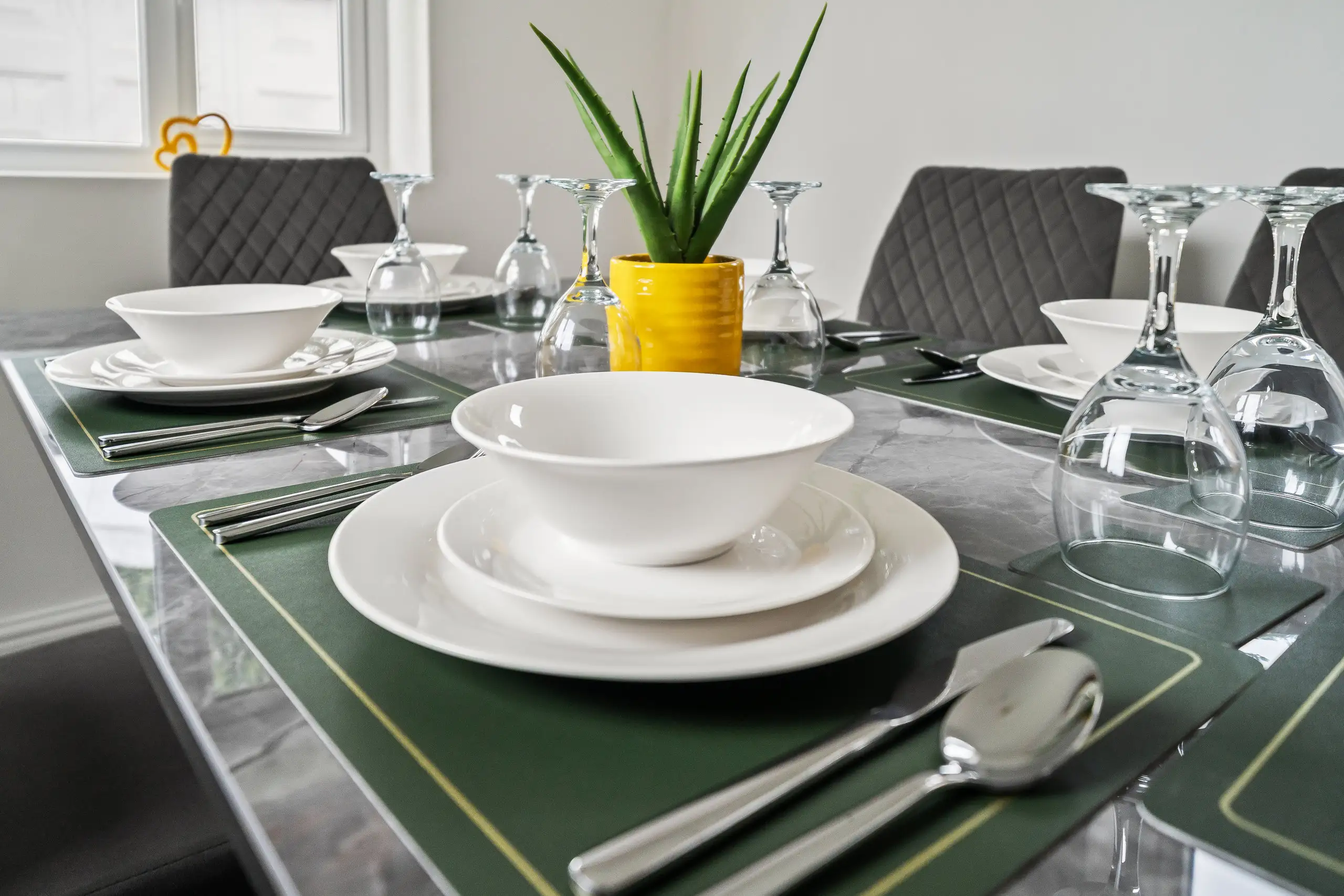 Close view of a place setting with white bowls, upturned wine glasses and green place mats