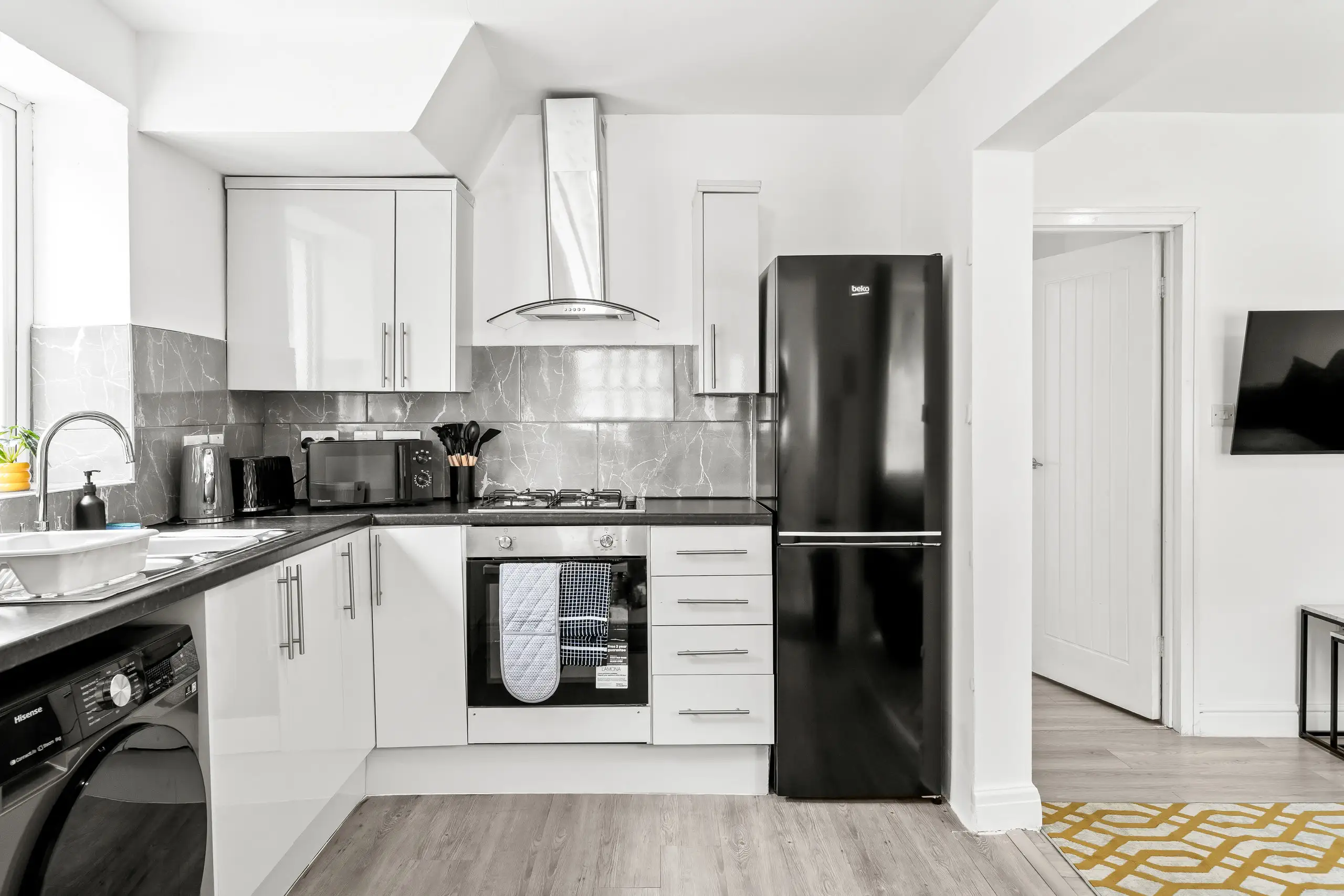 White gloss kitchen with a grey marble-effect splashback, black fridge freezer and washing machine
