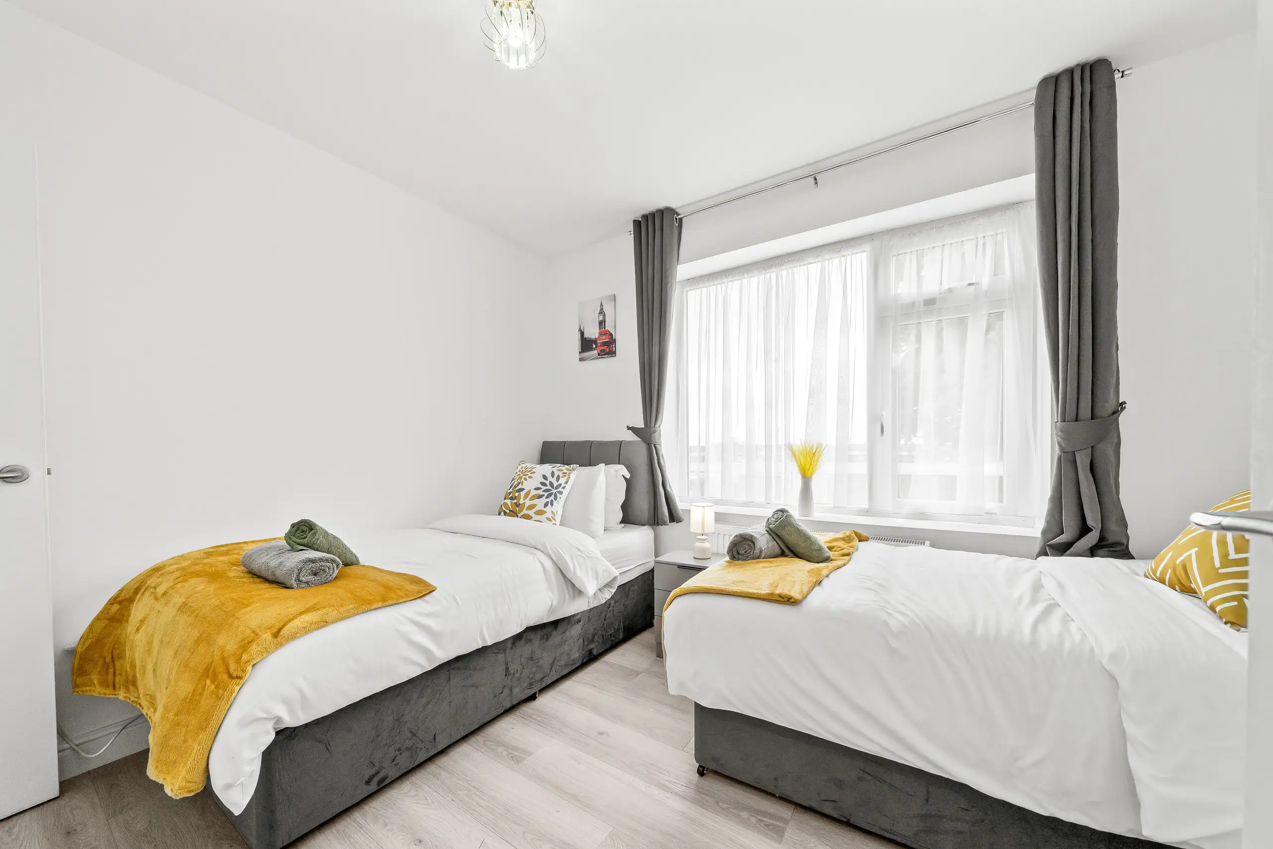 Twin bedroom with mustard throws, rolled towels and grey curtains