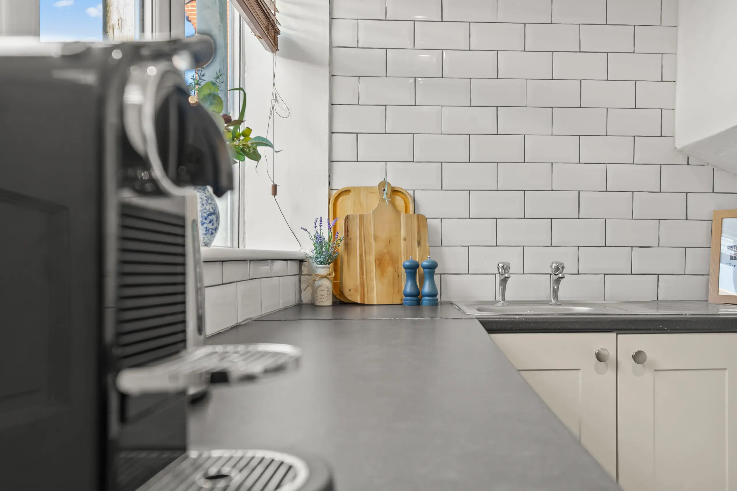 Coffee machine in the foreground of a kitchen with white metro tiles and wooden chopping boards
