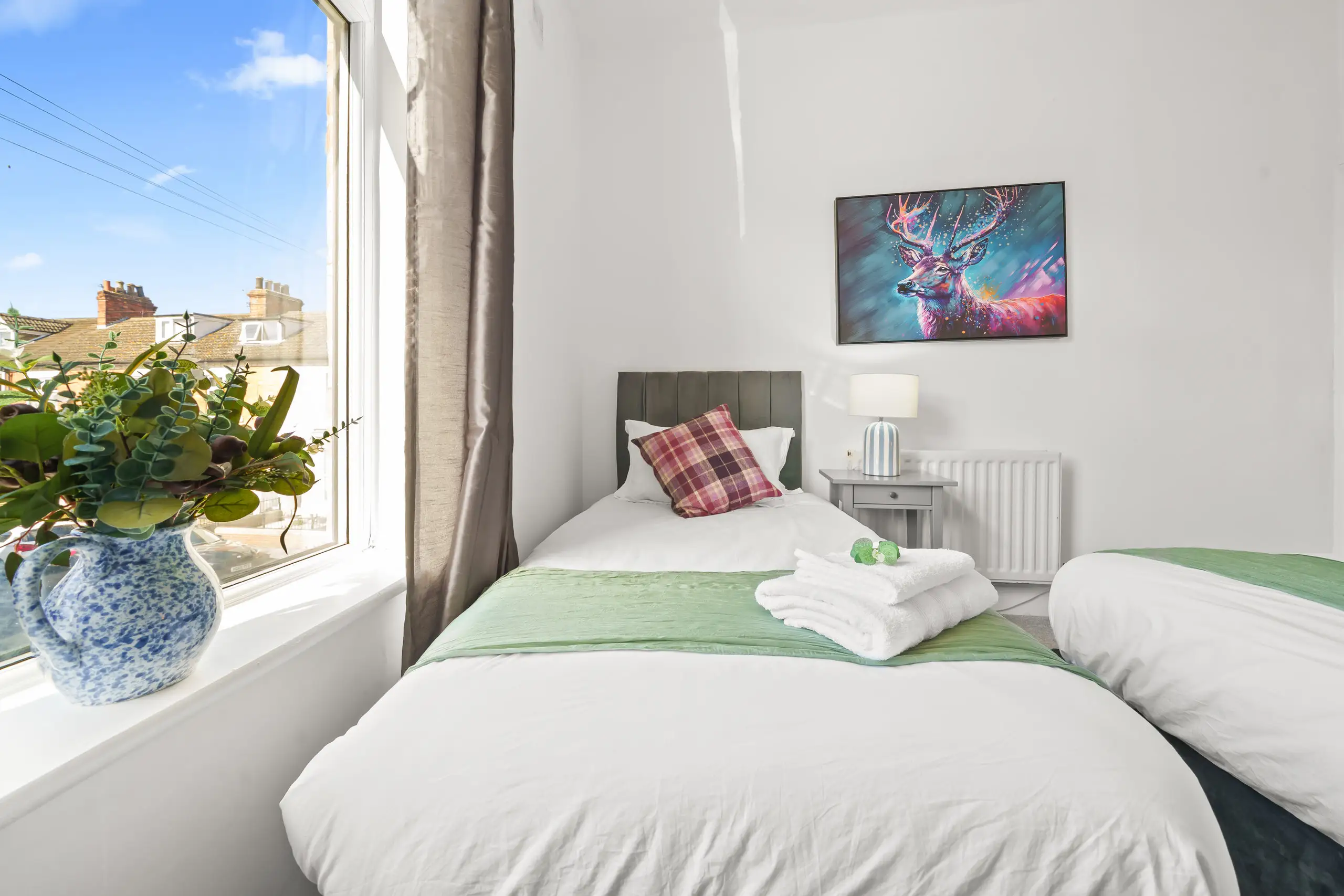 Twin bedroom with green bed runners, a tartan cushion and flowers on the windowsill