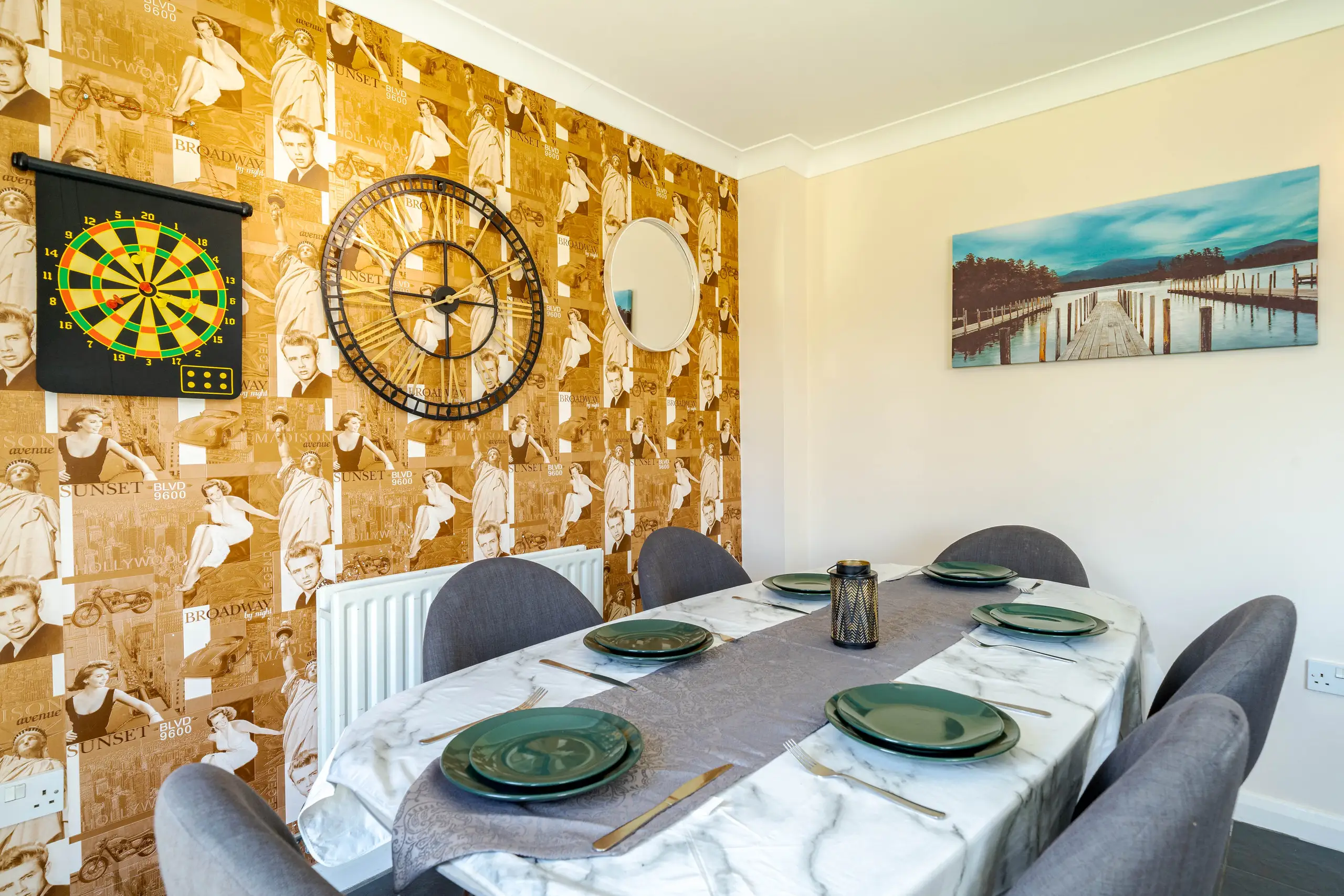 Dining table for six beside a feature wall of vintage film wallpaper and a large clock