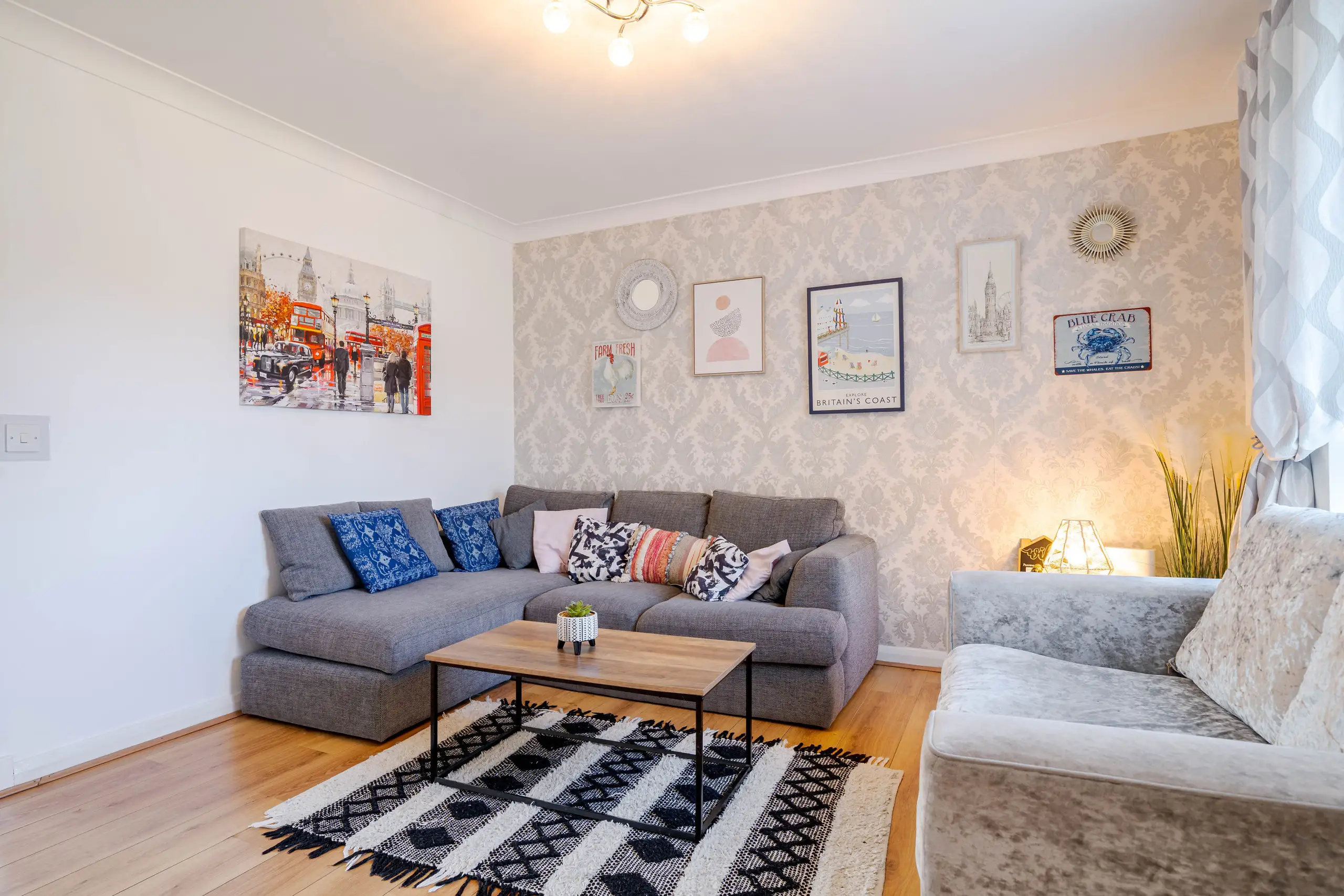 Living room with a grey corner sofa, patterned rug, damask feature wall and framed prints
