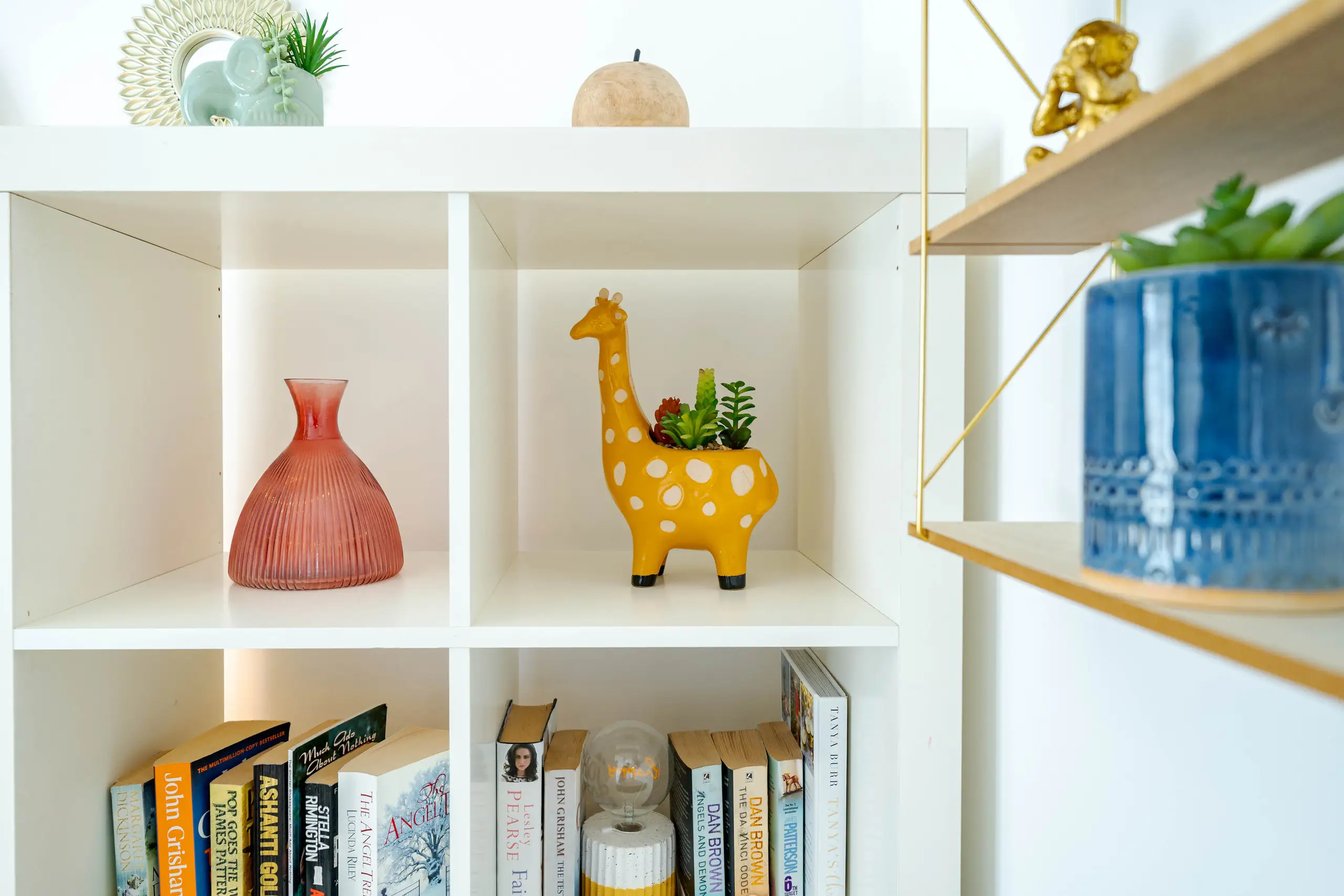 Bookcase detail with a giraffe planter, glass vase and paperbacks
