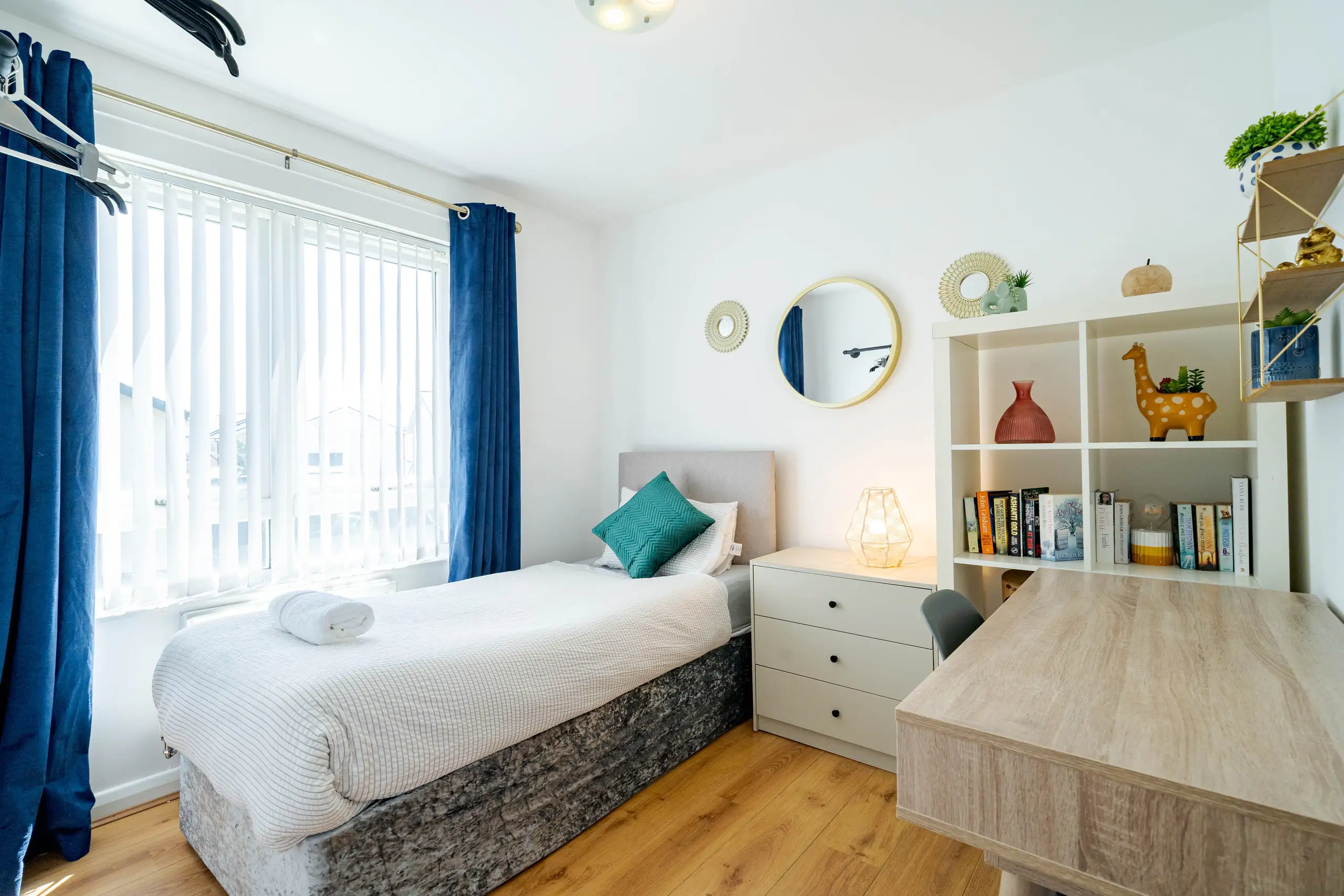 Single bedroom with a desk, bookcase, navy curtains and a teal cushion