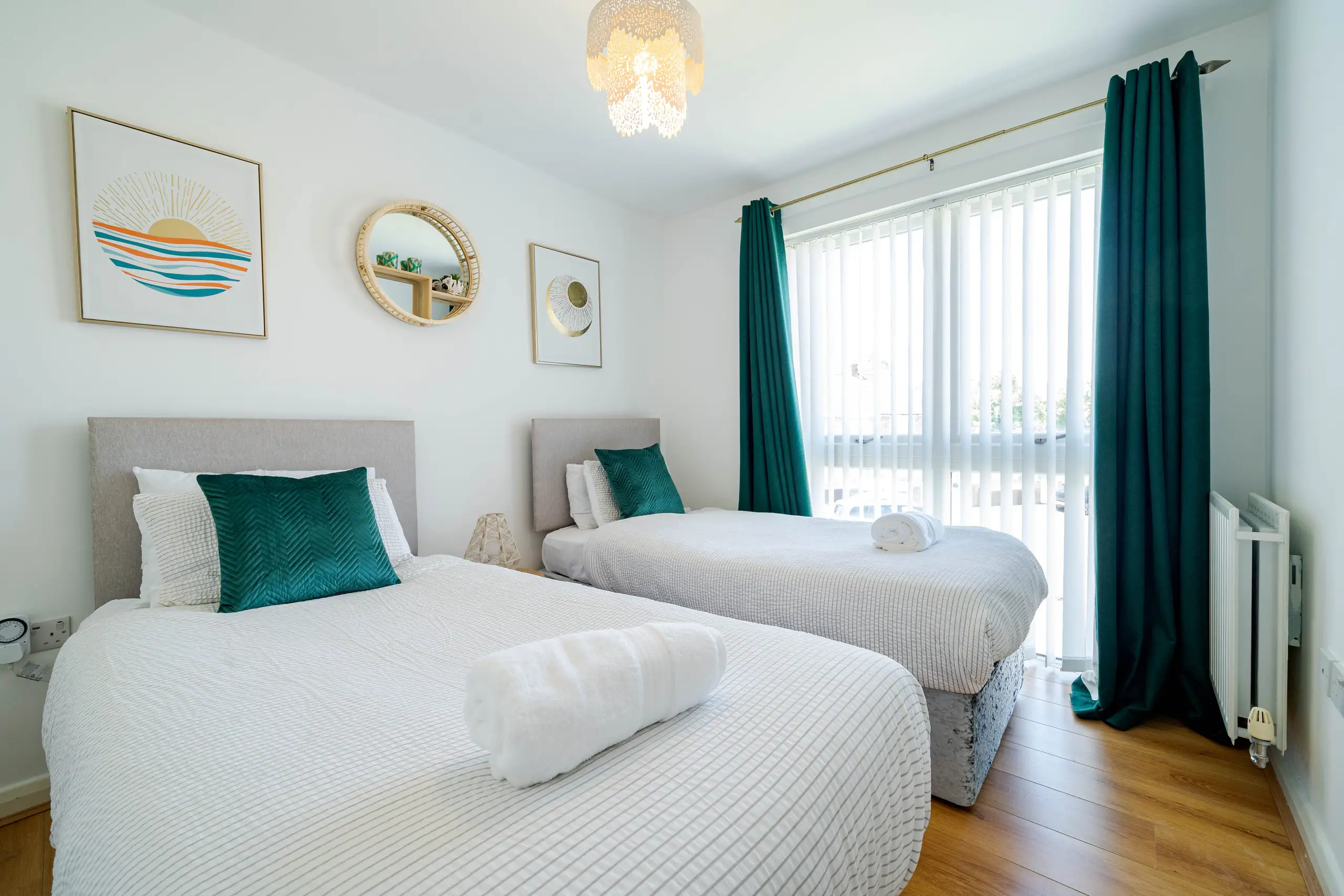 Twin bedroom with teal cushions, a rolled towel and teal curtains